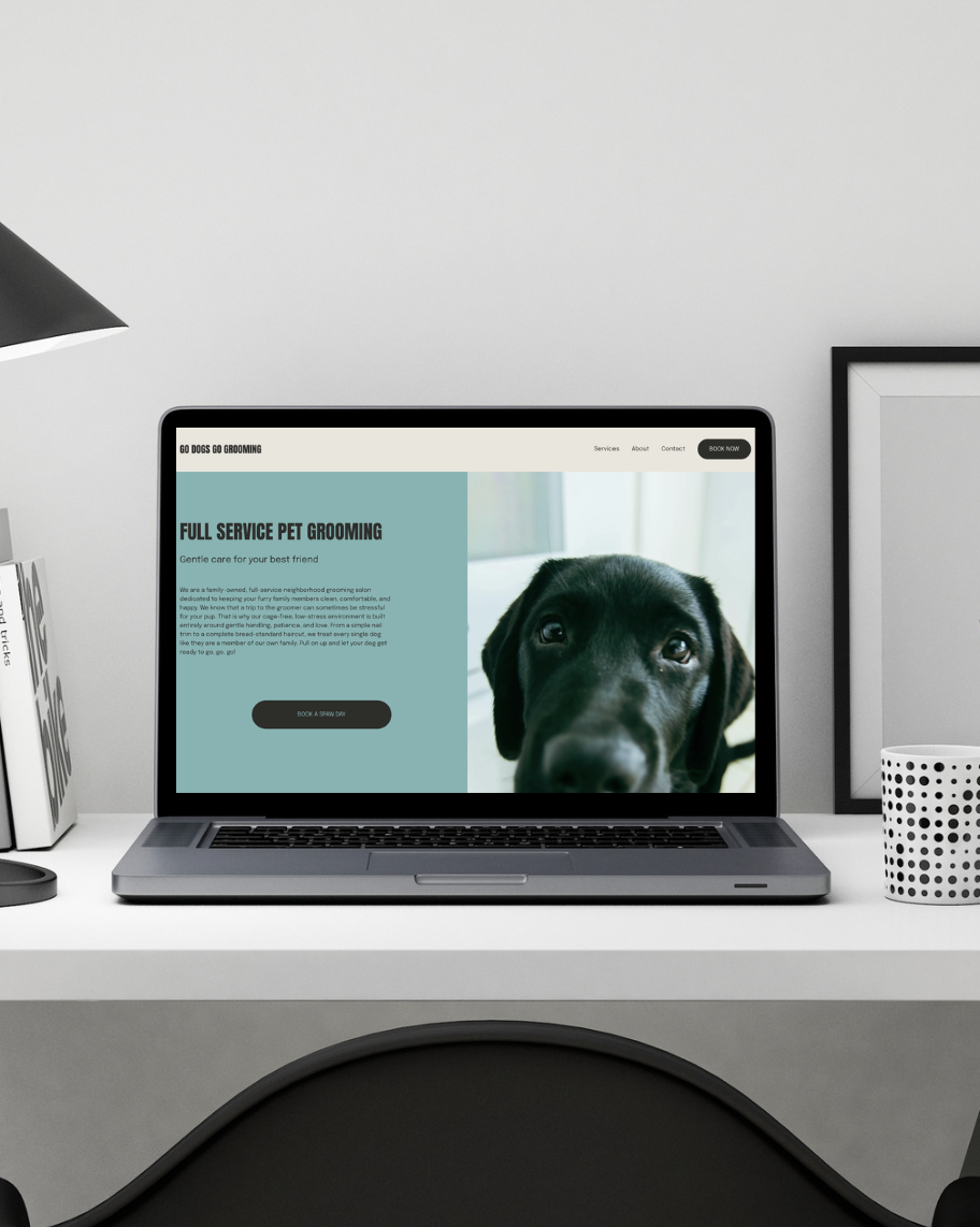 Laptop on white desk displaying a pet grooming website with a picture of a black puppy.