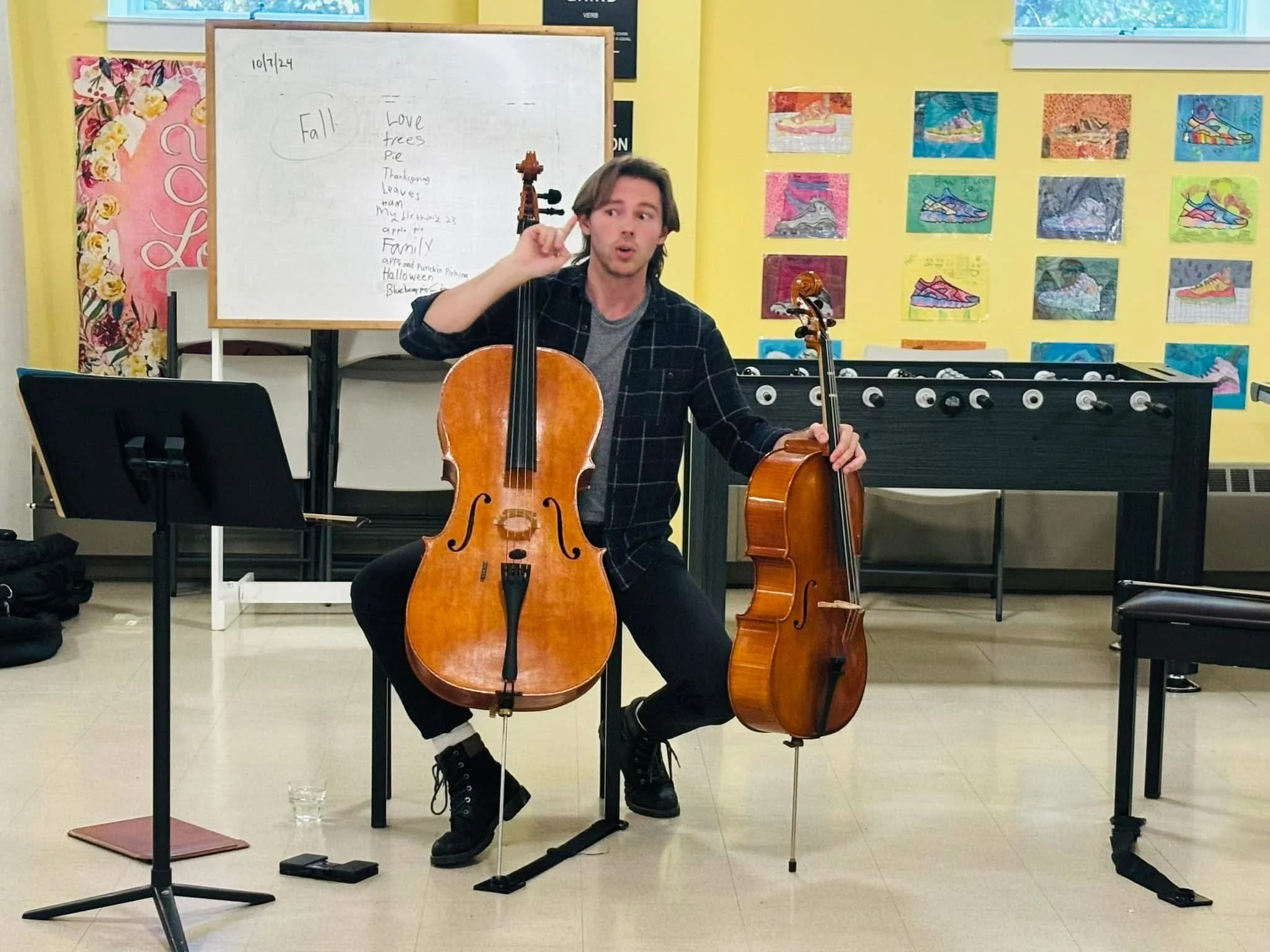 Nicholas Johnson playing cello and demonstrating cello during a group class, holding both a full size and eighth size cello.