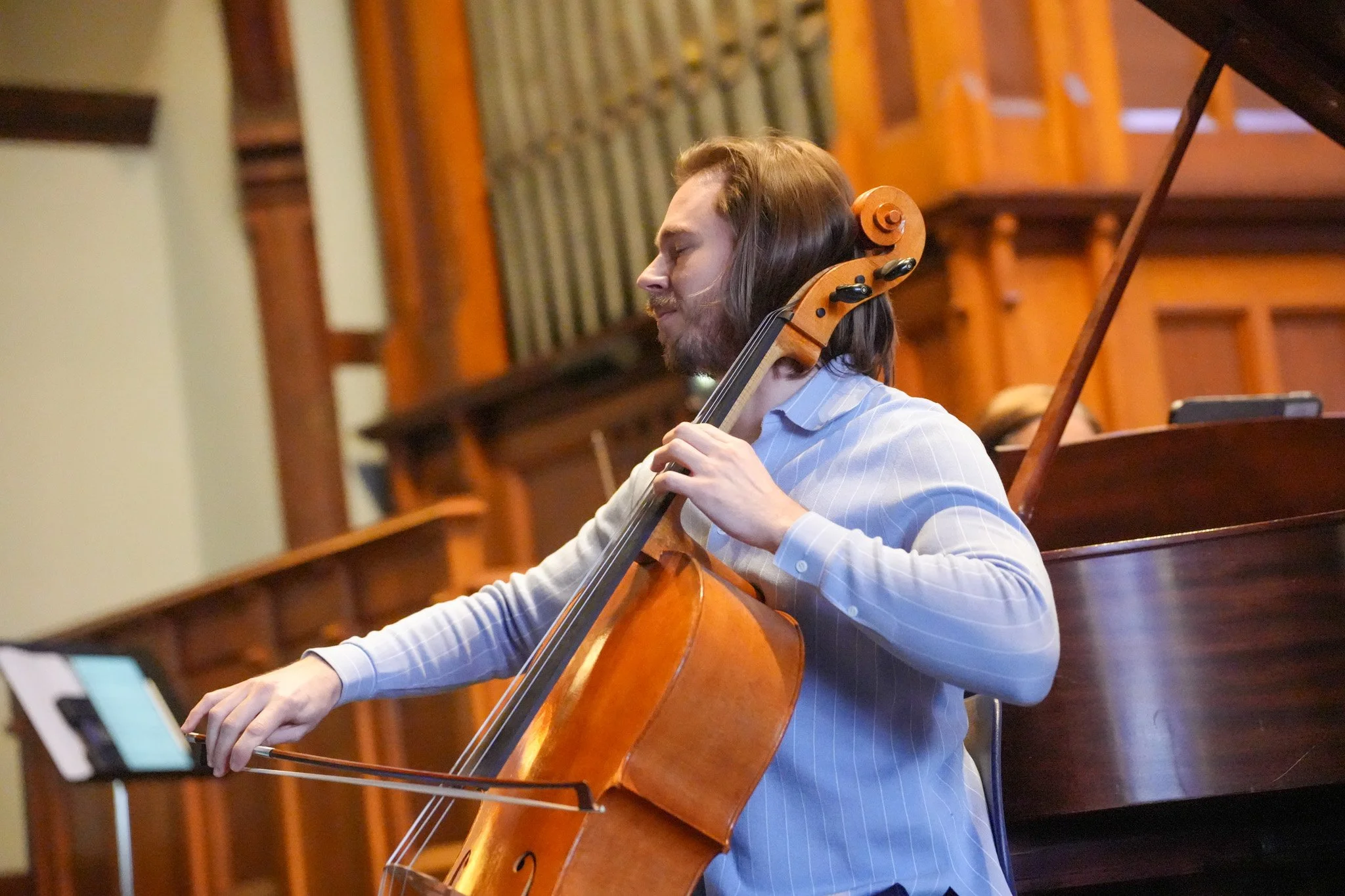 Nicholas Johnson playing cello during a performance in a wood-paneled room at Chapel Hill-Chauncy School