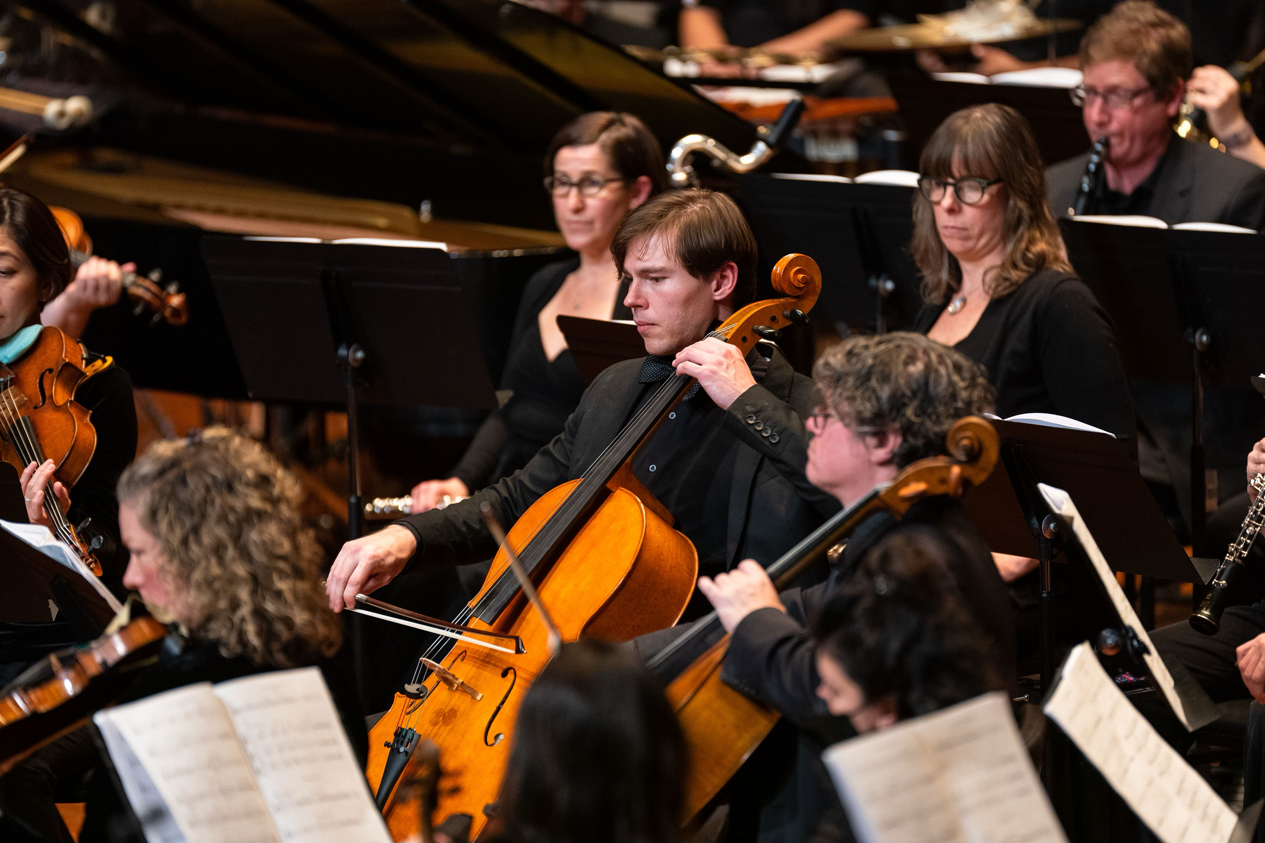Nicholas Johnson, Cello, performing in Boston Modern Orchestra Project (BMOP) alongside other musicians with sheet music in front of them.