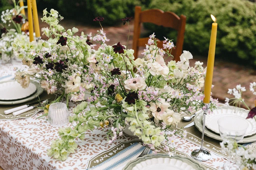 A decorated outdoor dining table with floral centerpiece, candles, and tableware.