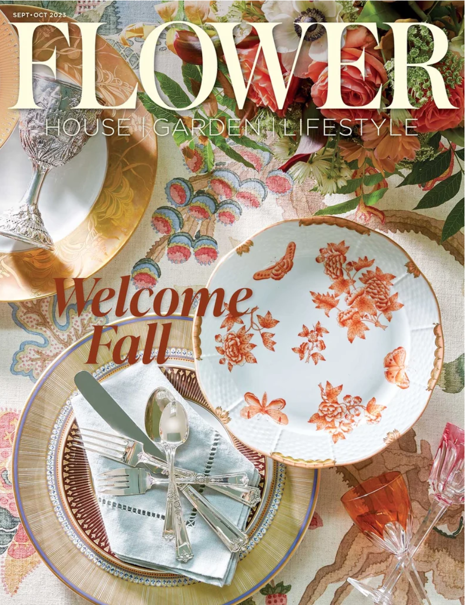 Table setting with floral and autumn-themed dishware, glassware, and cutlery, decorated for fall, with a floral centerpiece and colorful tablecloth.