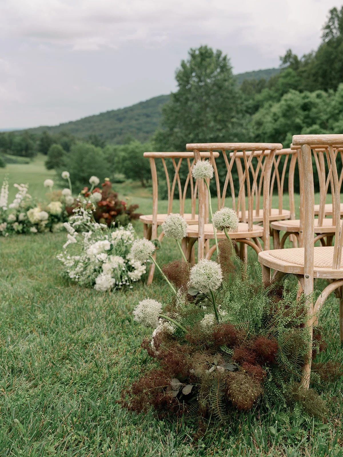 Wooden chairs arranged outdoors with floral arrangements and greenery in a scenic mountain setting.