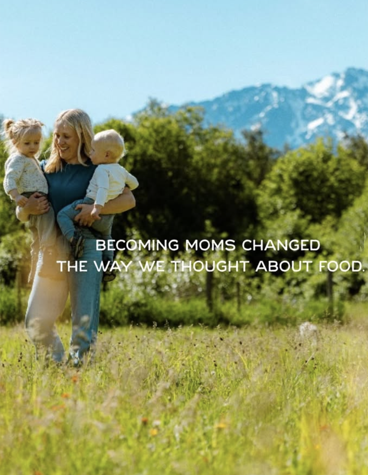 A mother holding her two young children outdoors with a mountain and trees in the background, with the text 'Becoming moms changed the way we thought about food' overlayed.