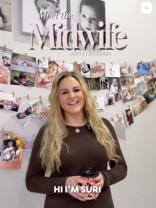 Woman with long blonde hair smiling, holding a cup, standing in front of a wall decorated with photos of babies and kids, and a sign that says 'Meet the Midwife Suri Friedman'.