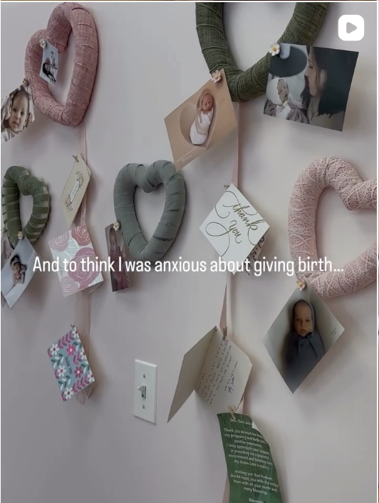 A wall decorated with pastel-colored heart-shaped yarn wreaths, photographs, and handwritten notes. One note says 'Thank You,' and another has a handwritten message. The photographs feature babies and a woman. The image includes an on-screen caption reading, 'And to think I was anxious about giving birth...'.