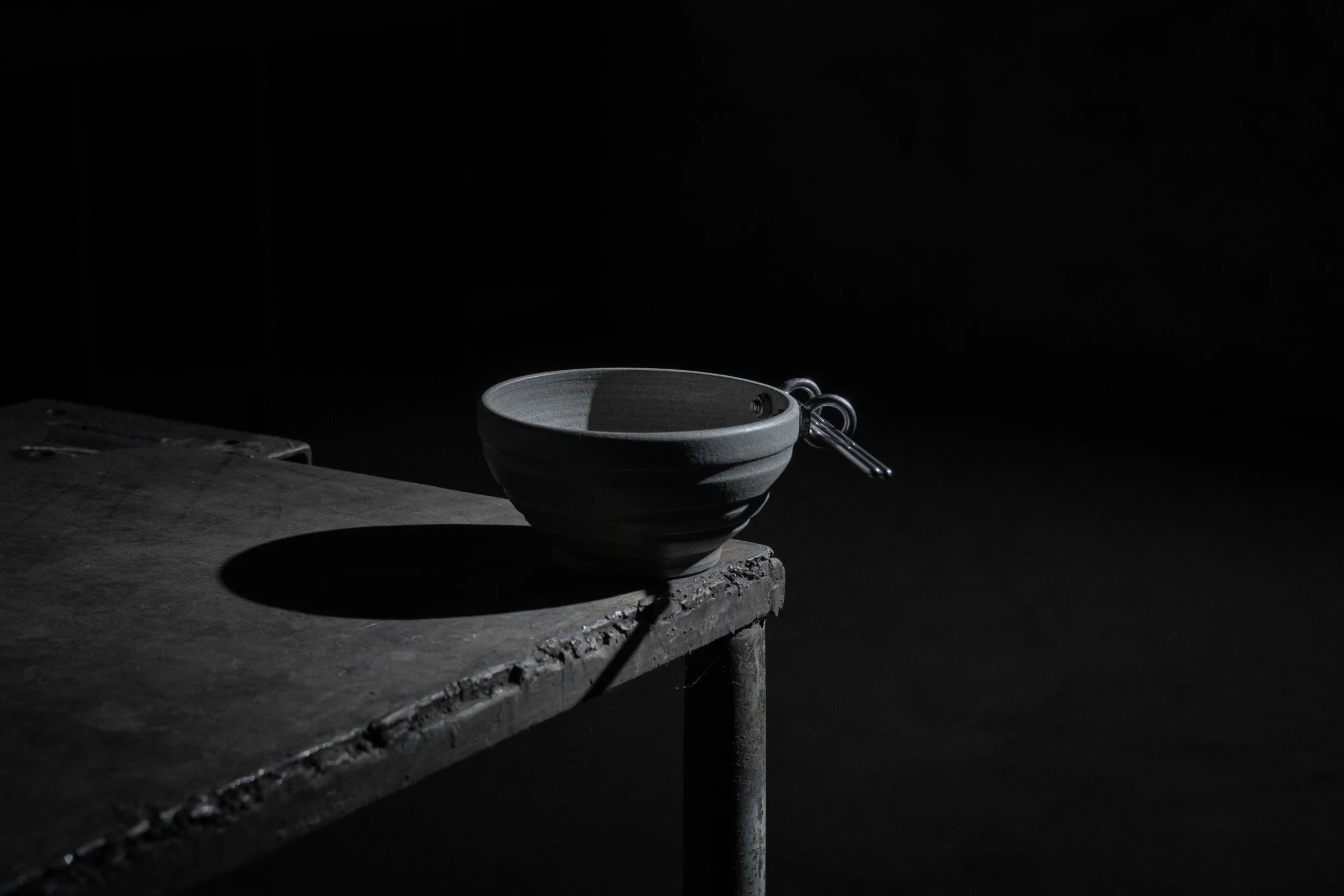 beton bowl in grey stoneware with chopsticks resting in its steel eye-bolt handle, on a worn table