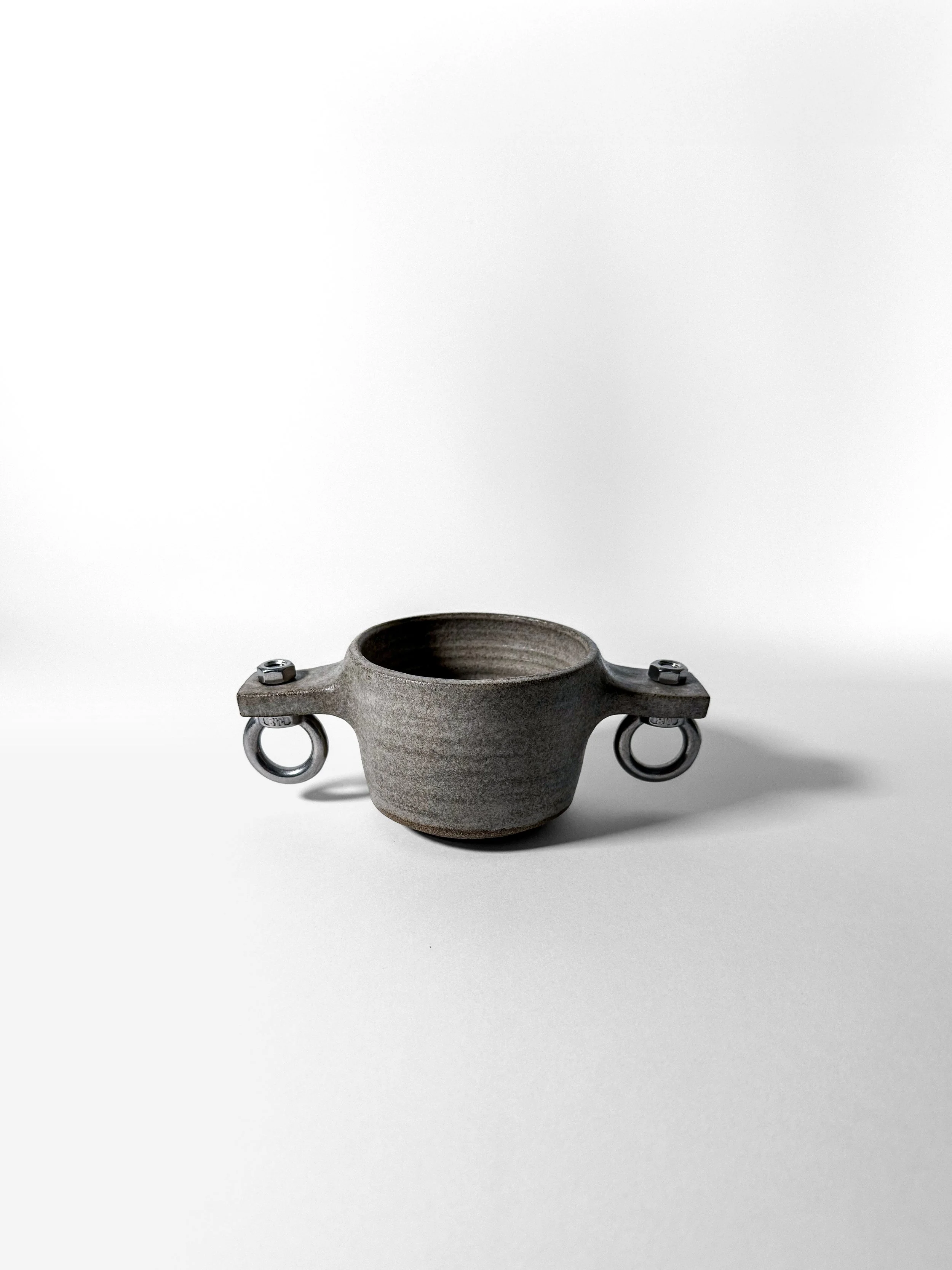 brutalist love handmade stoneware cup with symmetrical steel eye-bolt handles, three-quarter view