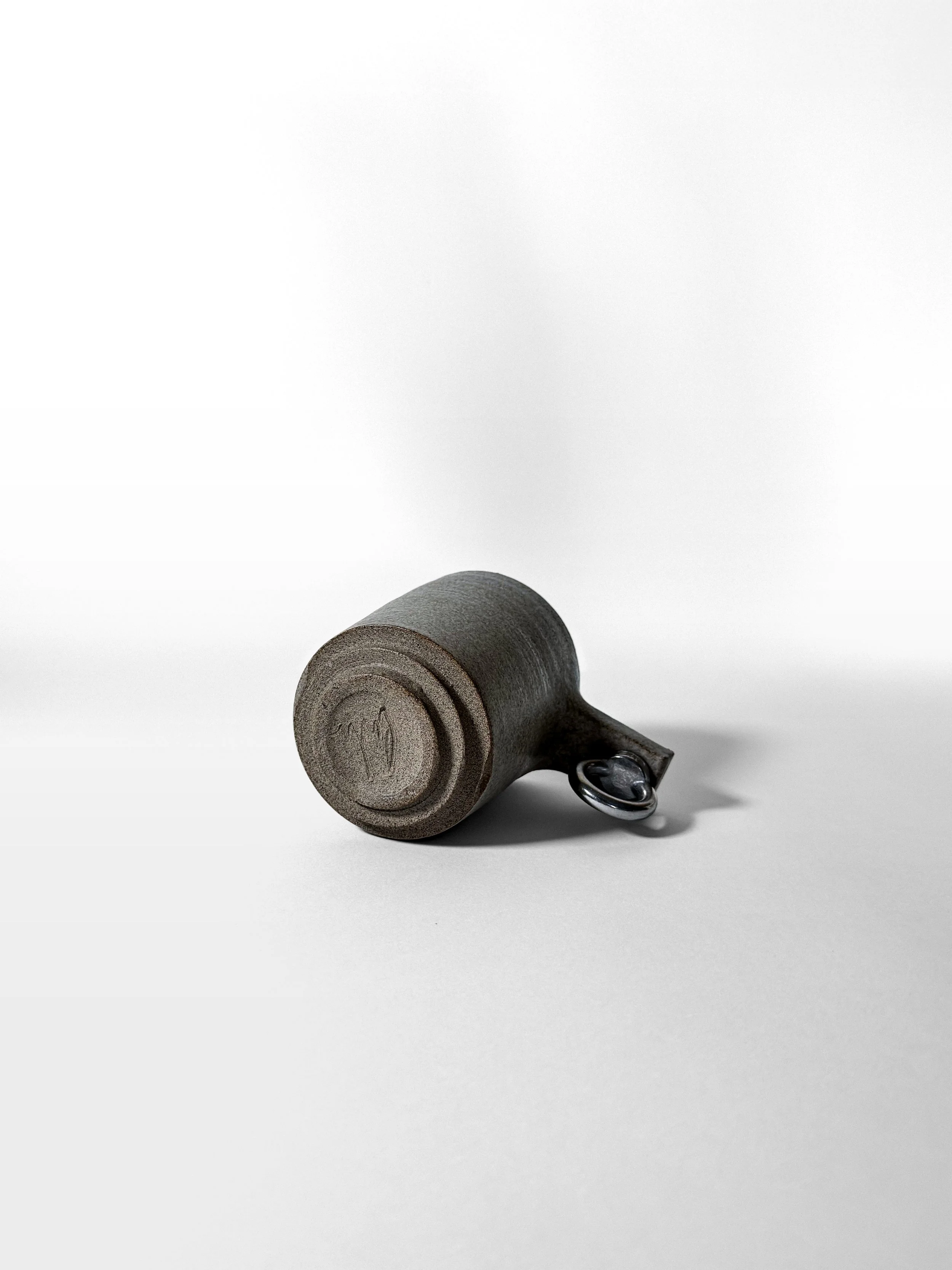 brutalist mug lying on its side, showing the wheel-thrown foot and steel handle