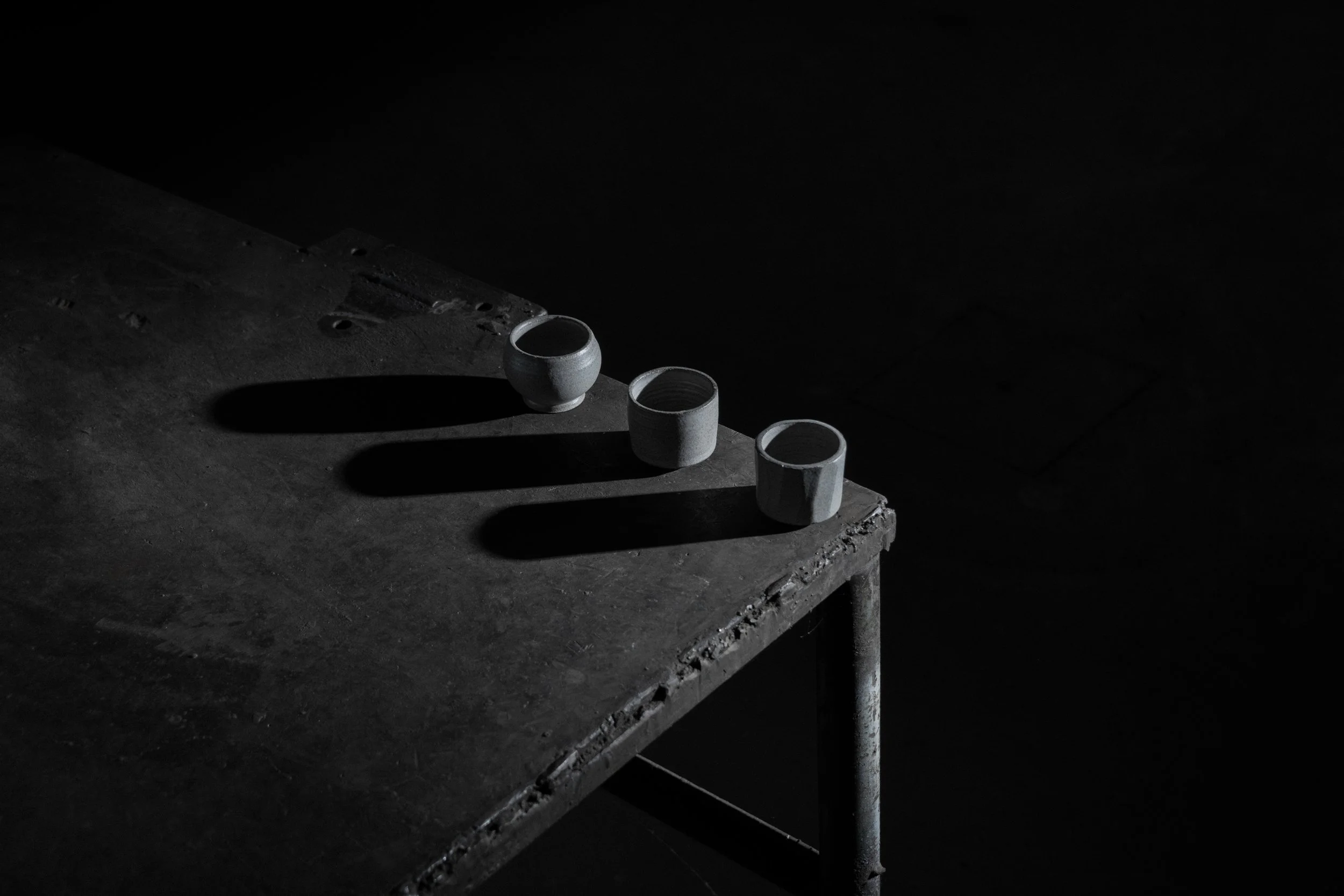 three handmade brutalist stoneware espresso cups on a worn steel table, black and white