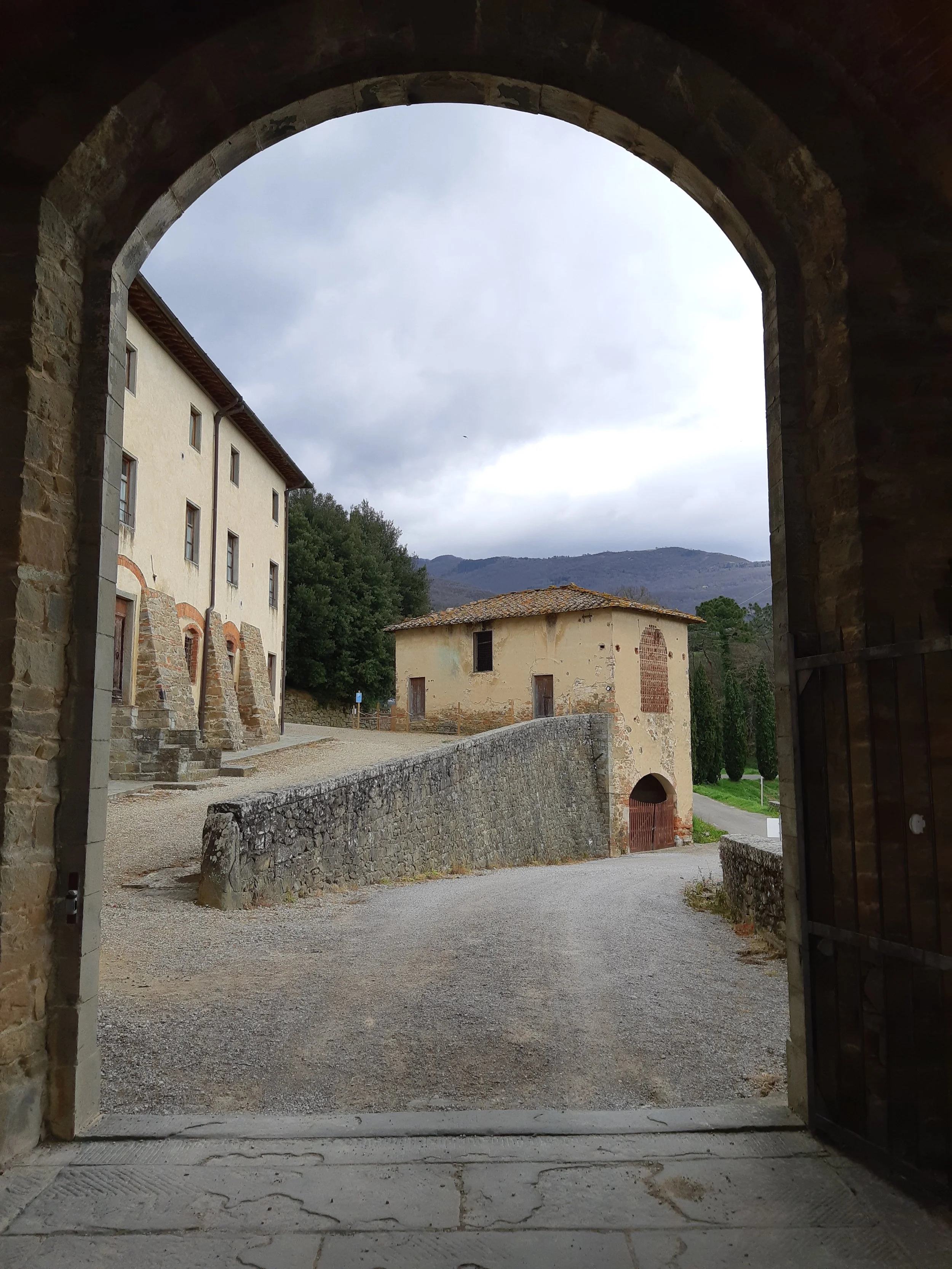 View of old buildings and landscape through a stone archway, with cloudy sky and mountains in the background.