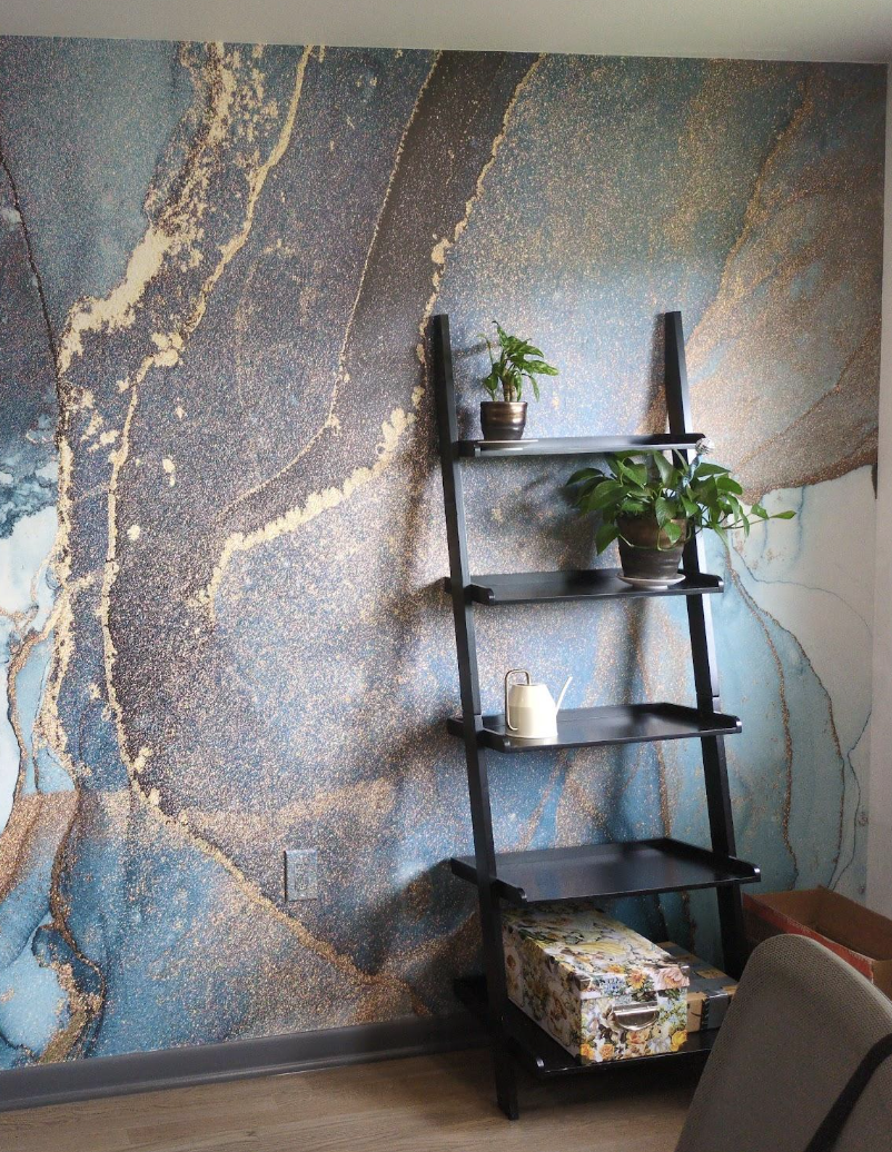 Black ladder-style shelf with potted plants and decorative accents against a textured blue and gold wall inside Dark Moon Counseling.