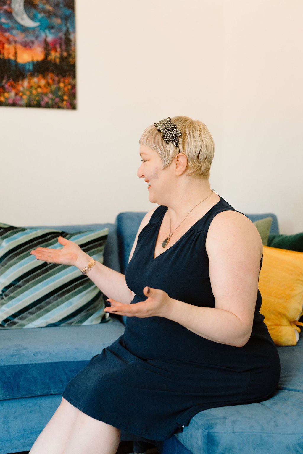 Omy Golden, licensed professional counselor, smiling and gesturing warmly while seated on a blue couch in her therapy office.