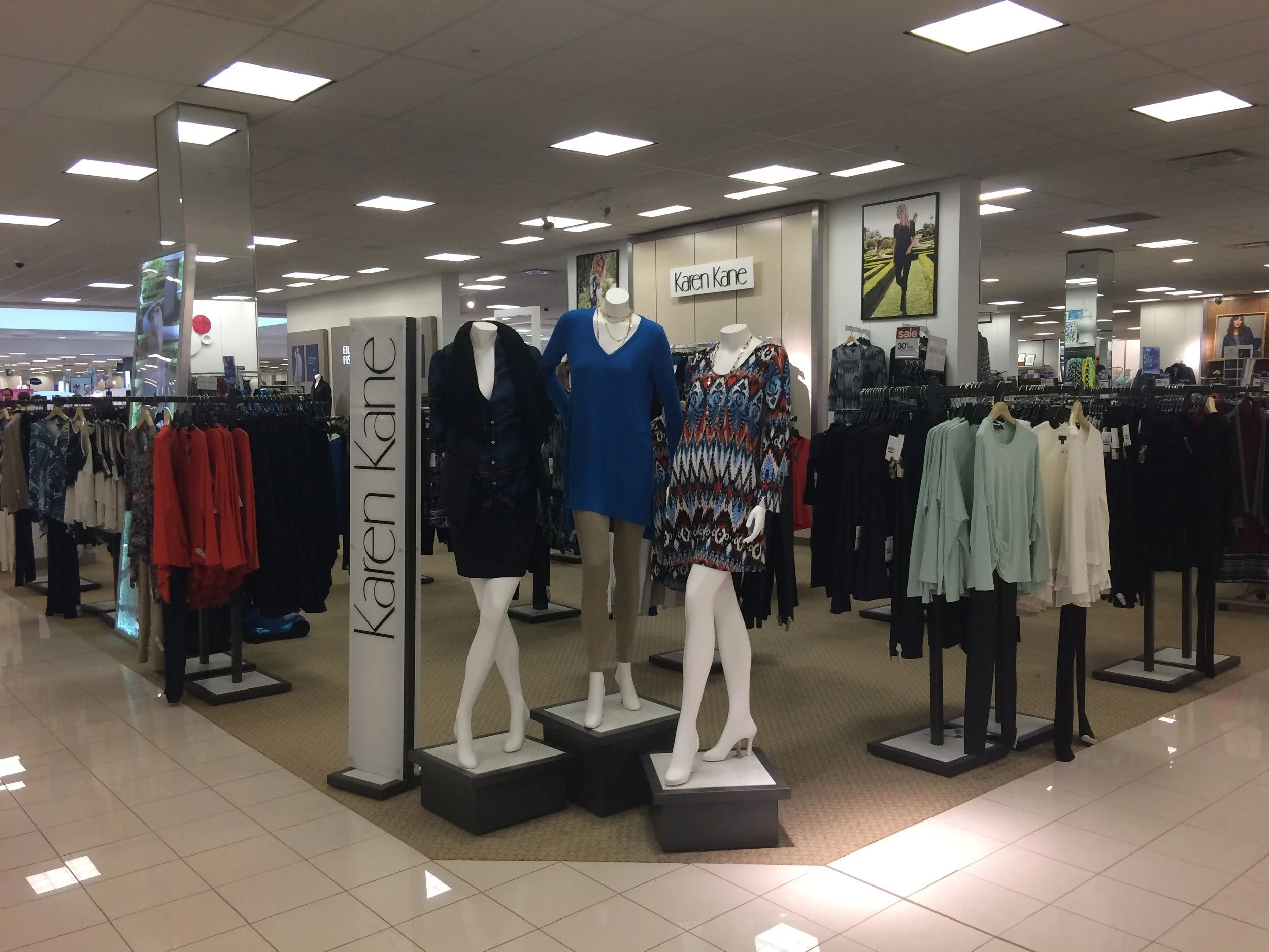 Mannequins dressed in women's clothing at a department store, with a sign reading 'Karen Kane' in the background.