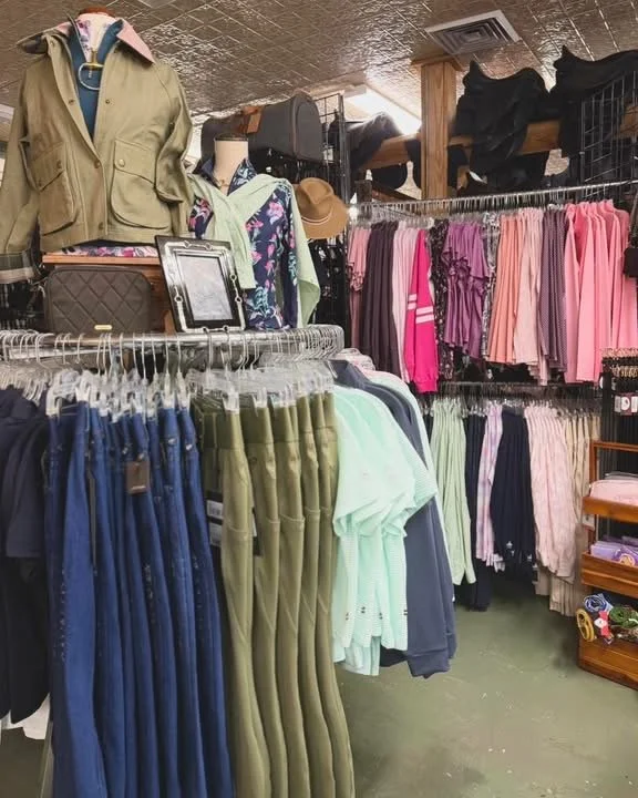 Clothing store with various garments on display, including pants, shirts, jackets, and accessories arranged on racks and shelves.