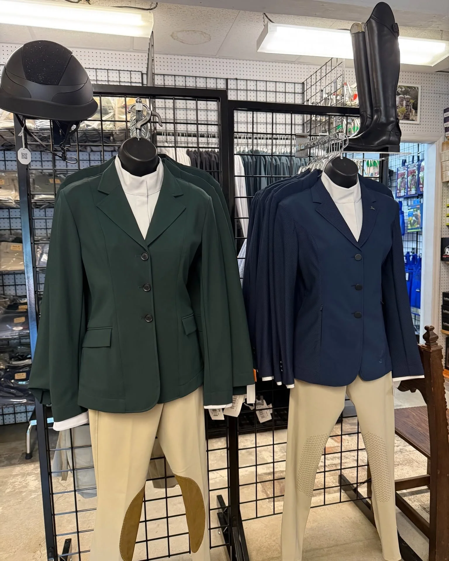 Display of mannequins dressed in blazers and pants, with helmets and boots on shelves in a retail store.