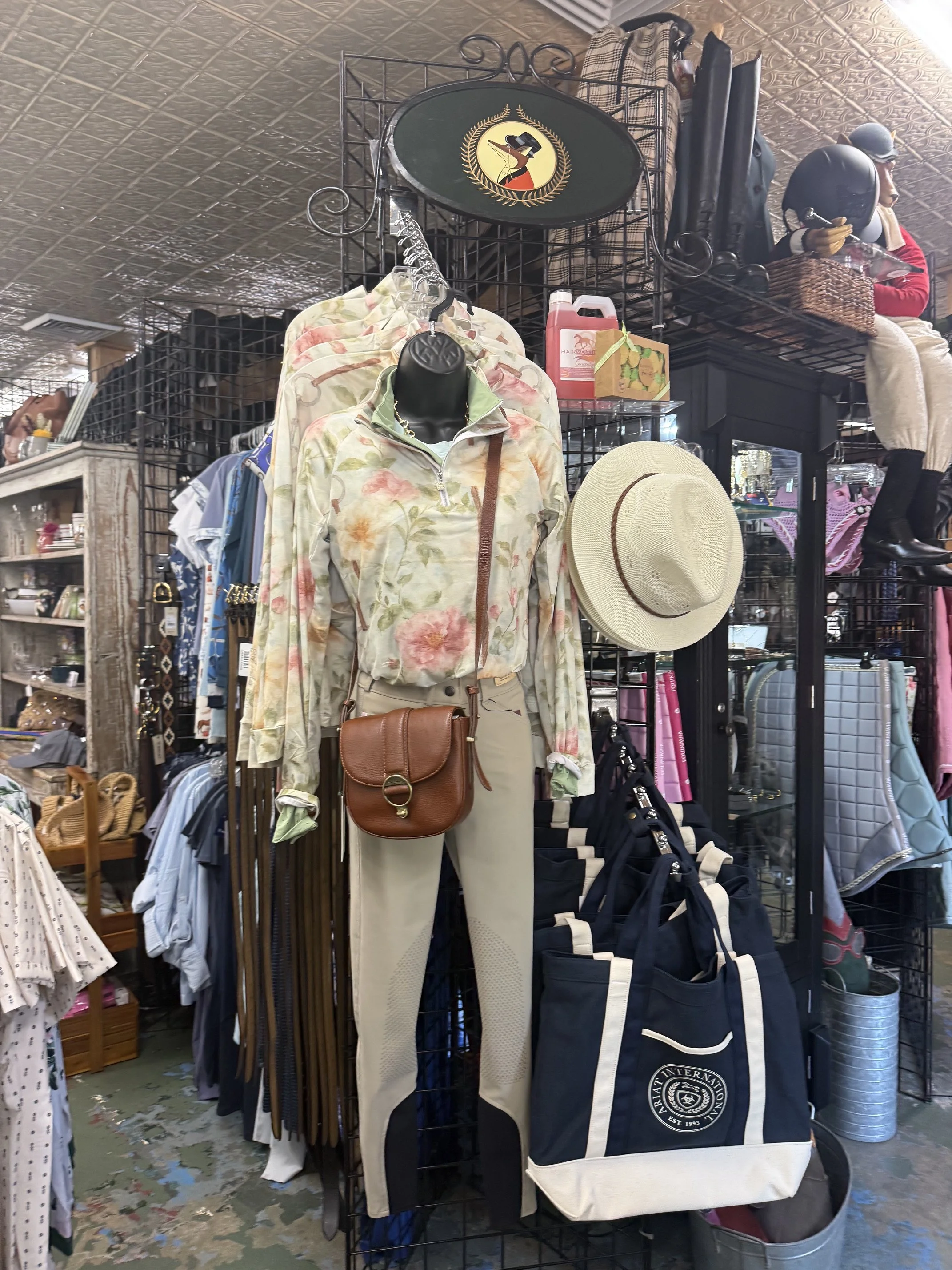 Clothing items, handbags, and accessories displayed on black metal shelves in a thrift store, including a floral jacket, a tan hat, and various bags.