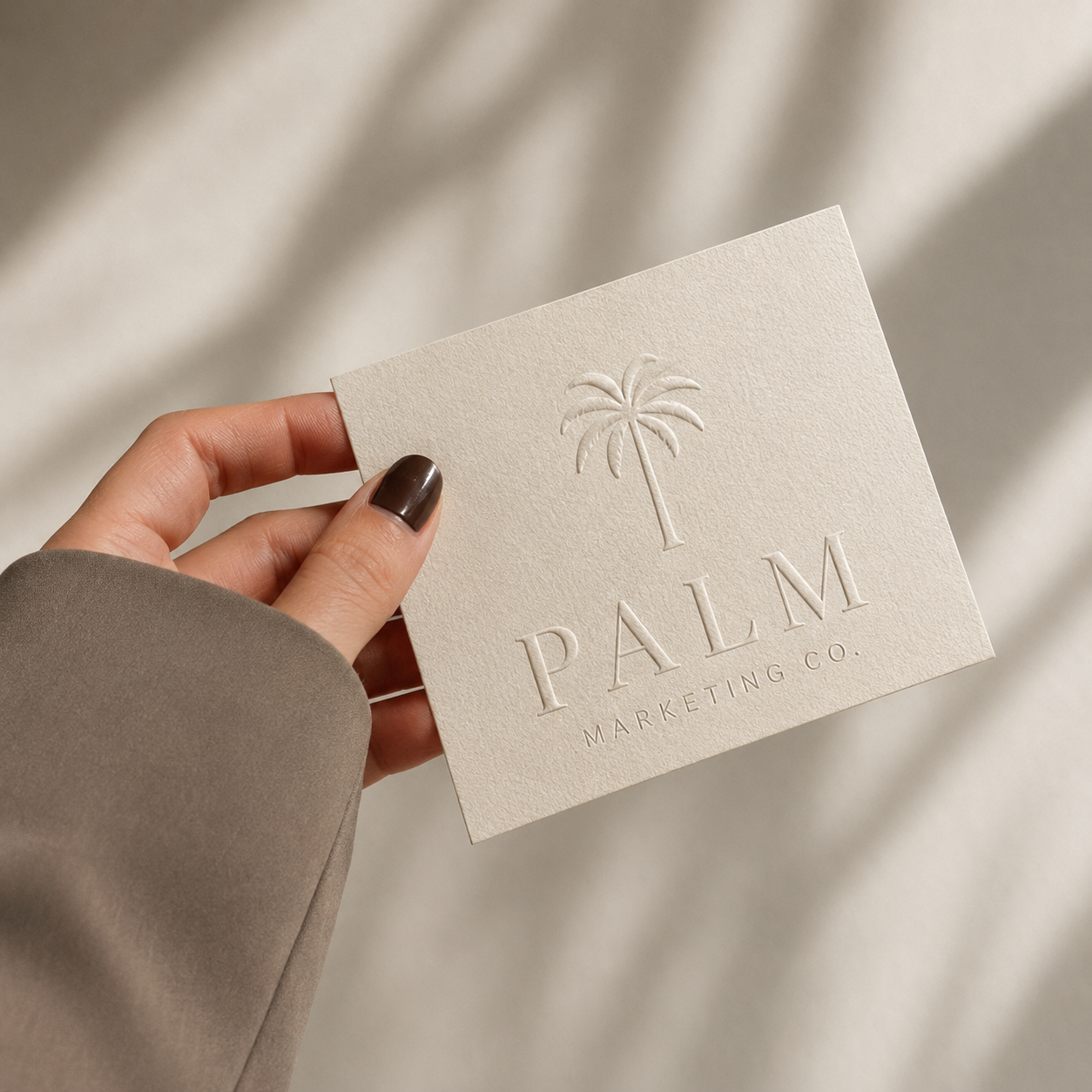 A hand holding a beige textured card with a palm tree embossed and the words 'PALM MARKETING CO.' printed below.