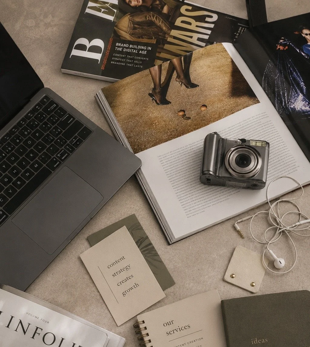 Desk with an open laptop, magazines, a camera, earphones, and notes related to content strategy and growth.