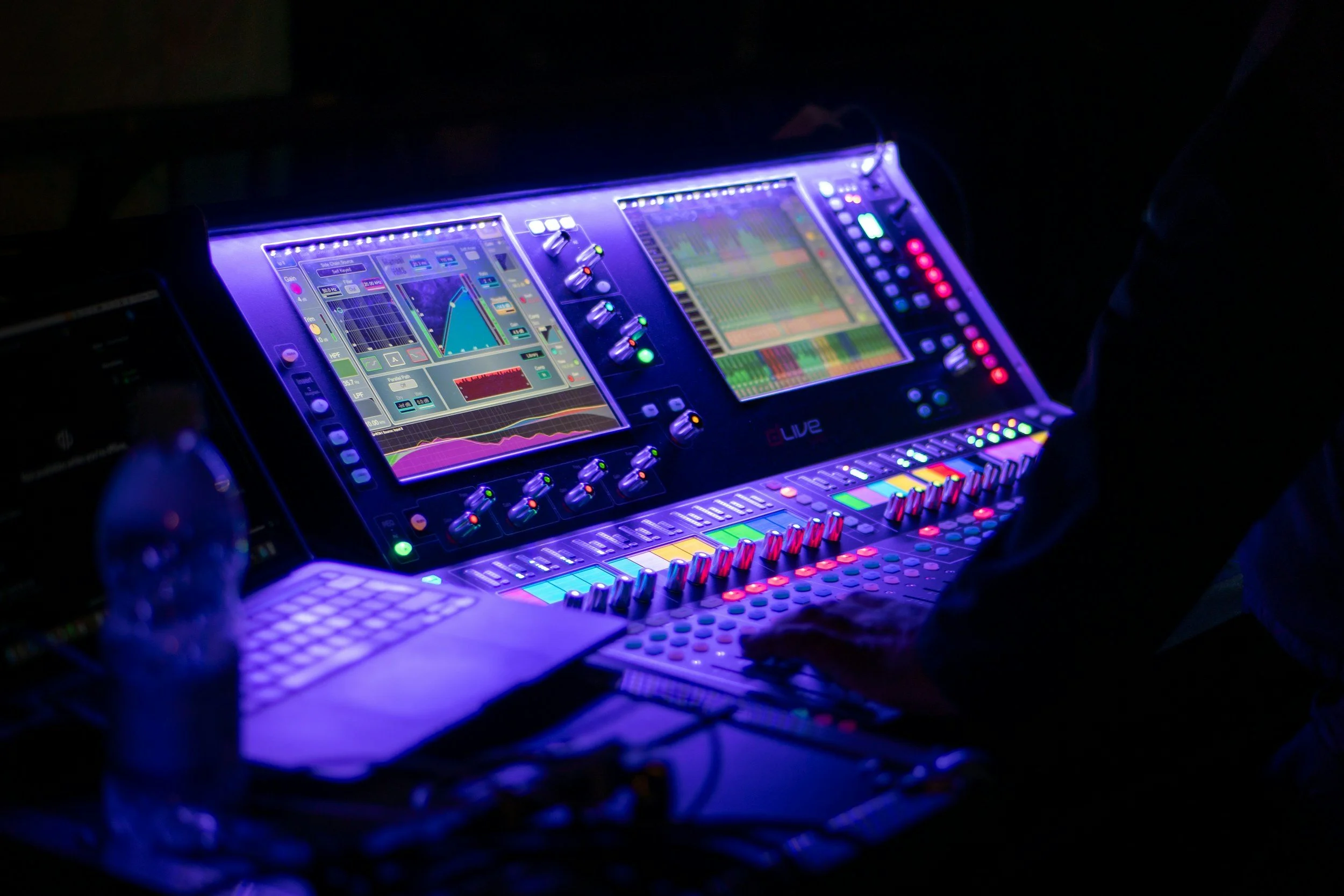 A DJ console with illuminated controls and screens displaying audio levels and waveforms in a dark setting.