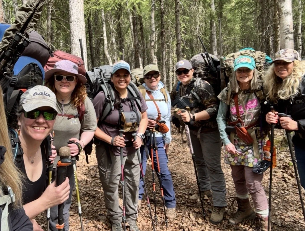 Group of women with backpacks and hiking gear standing on a forest trail.