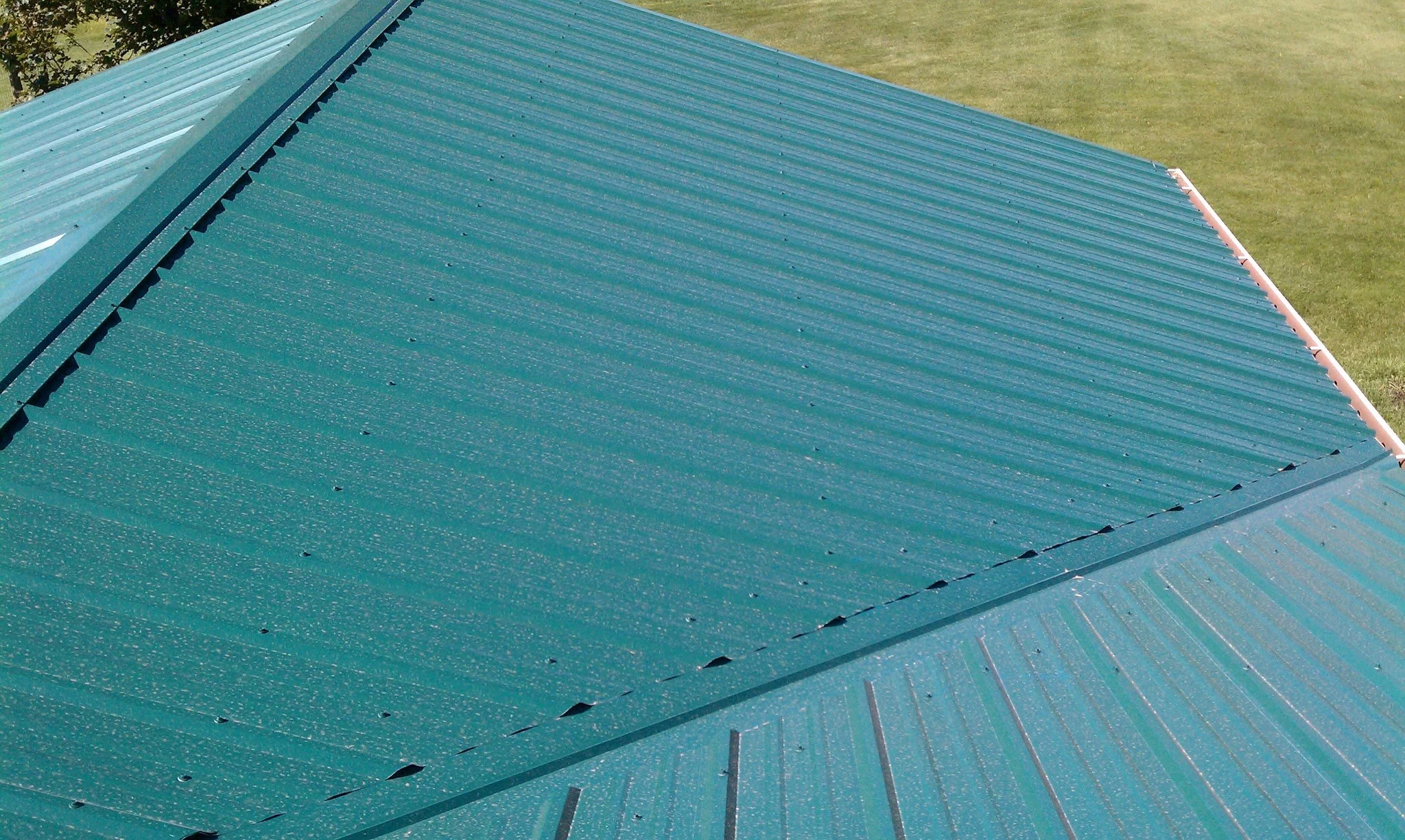 Close-up of a teal-colored metal roof with a grassy yard in the background.