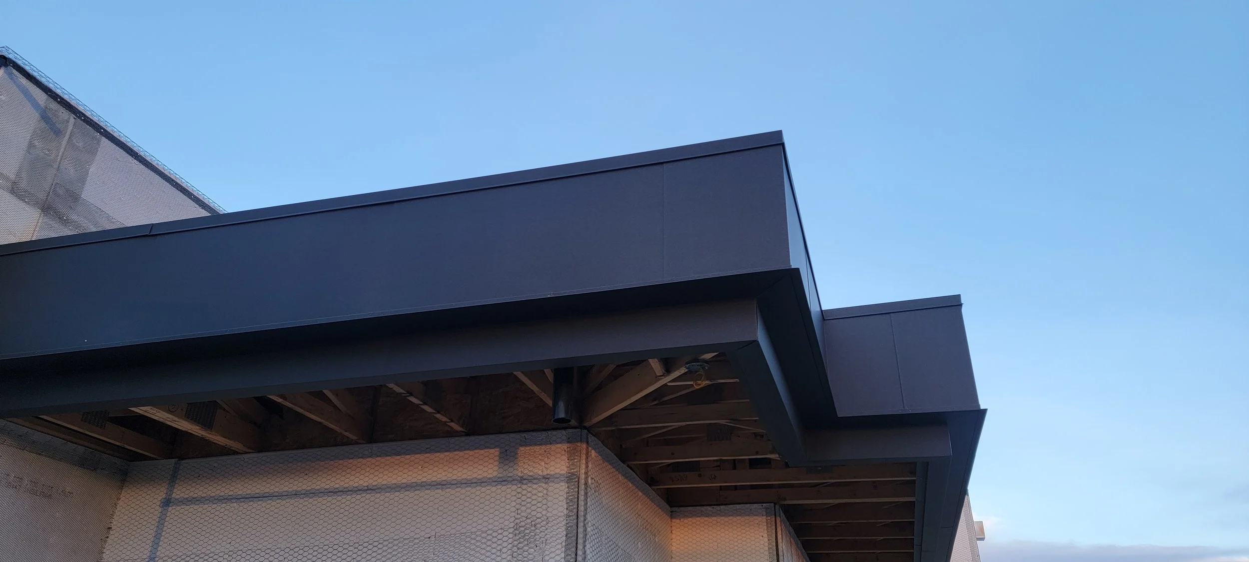Close-up of a modern building's corner with dark metal siding against a clear blue sky.