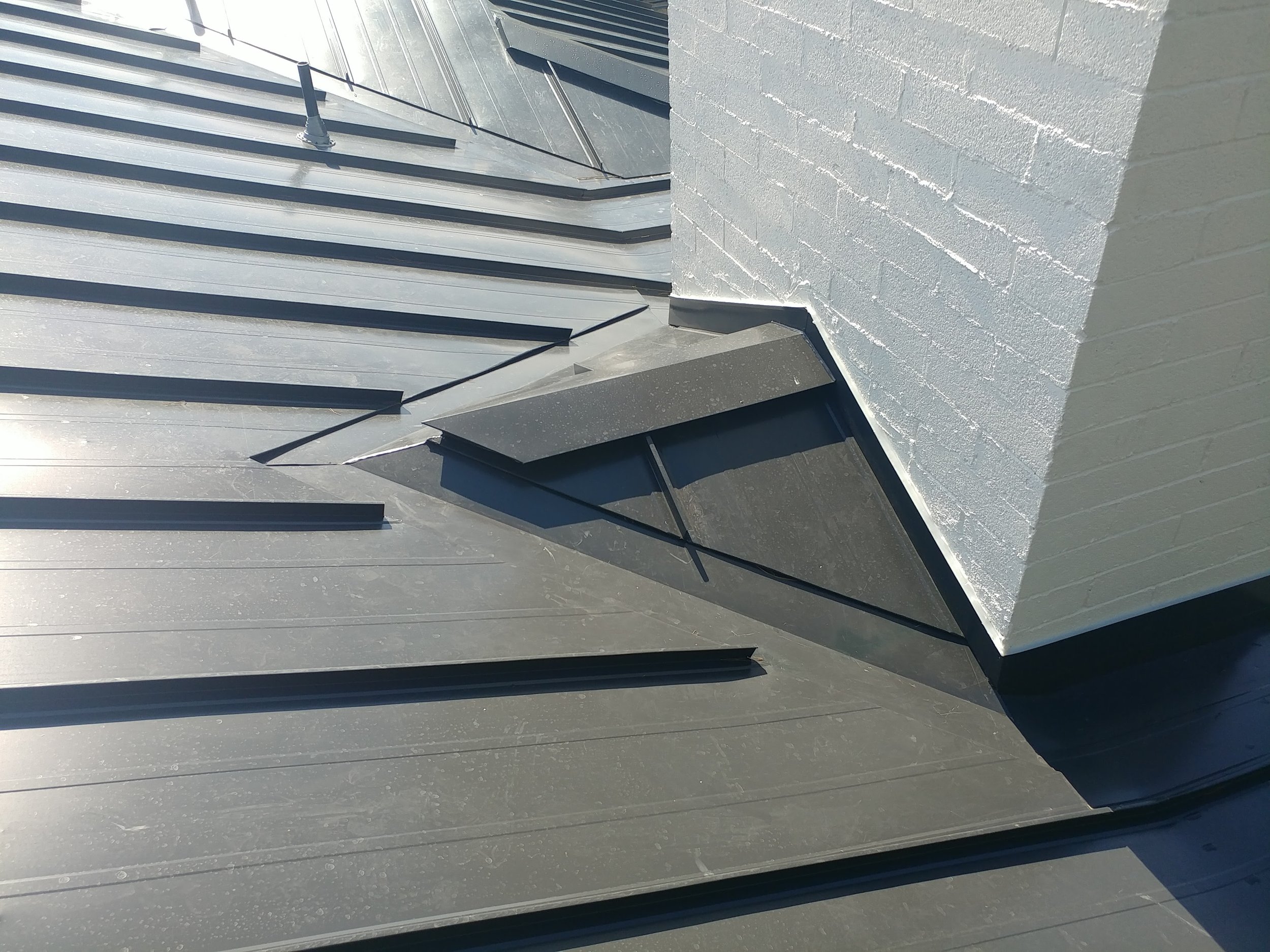 Close-up of a sloped metal roof with ridge vents and a white brick chimney on the right side.