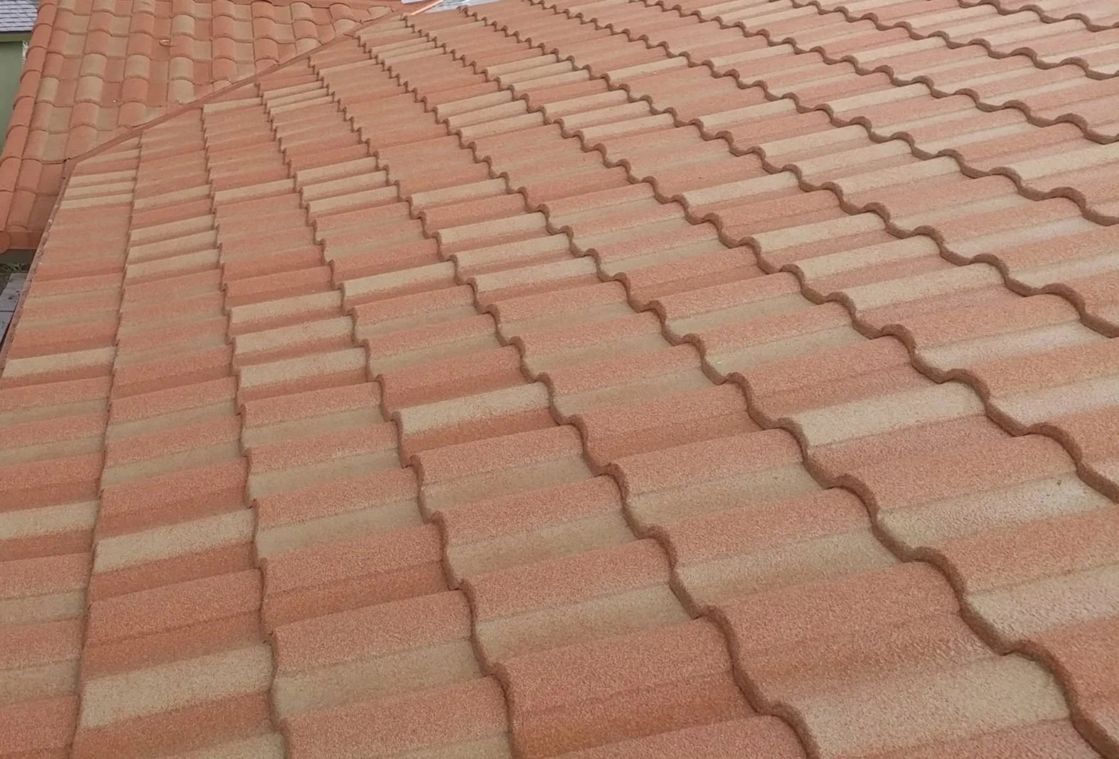 Close-up view of a sloped roof with orange and tan ceramic interlocking tiles.