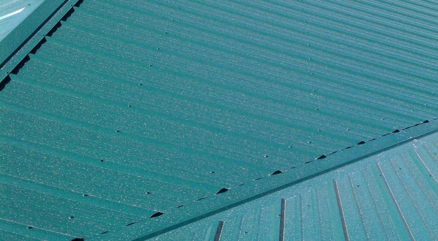 Close-up view of a green metal roof with evenly spaced screws and ridges.