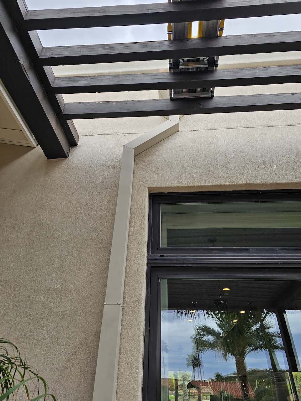 View of a building exterior with a window, an outdoor ceiling with slatted wooden panels, and a white downspout pipe.