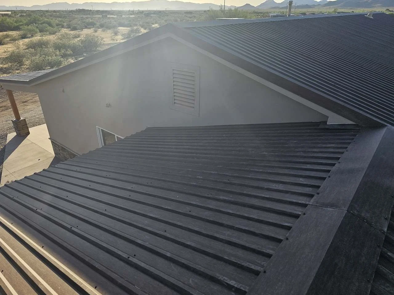 An aerial view of a house with a metal roof and a view of desert landscape and mountains in the background.