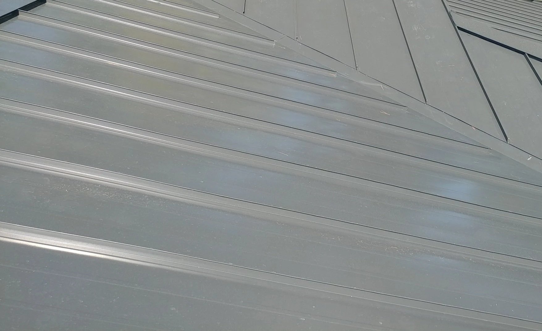 Close-up of metallic building panel with diagonal ridges and a triangular section in the top right corner.
