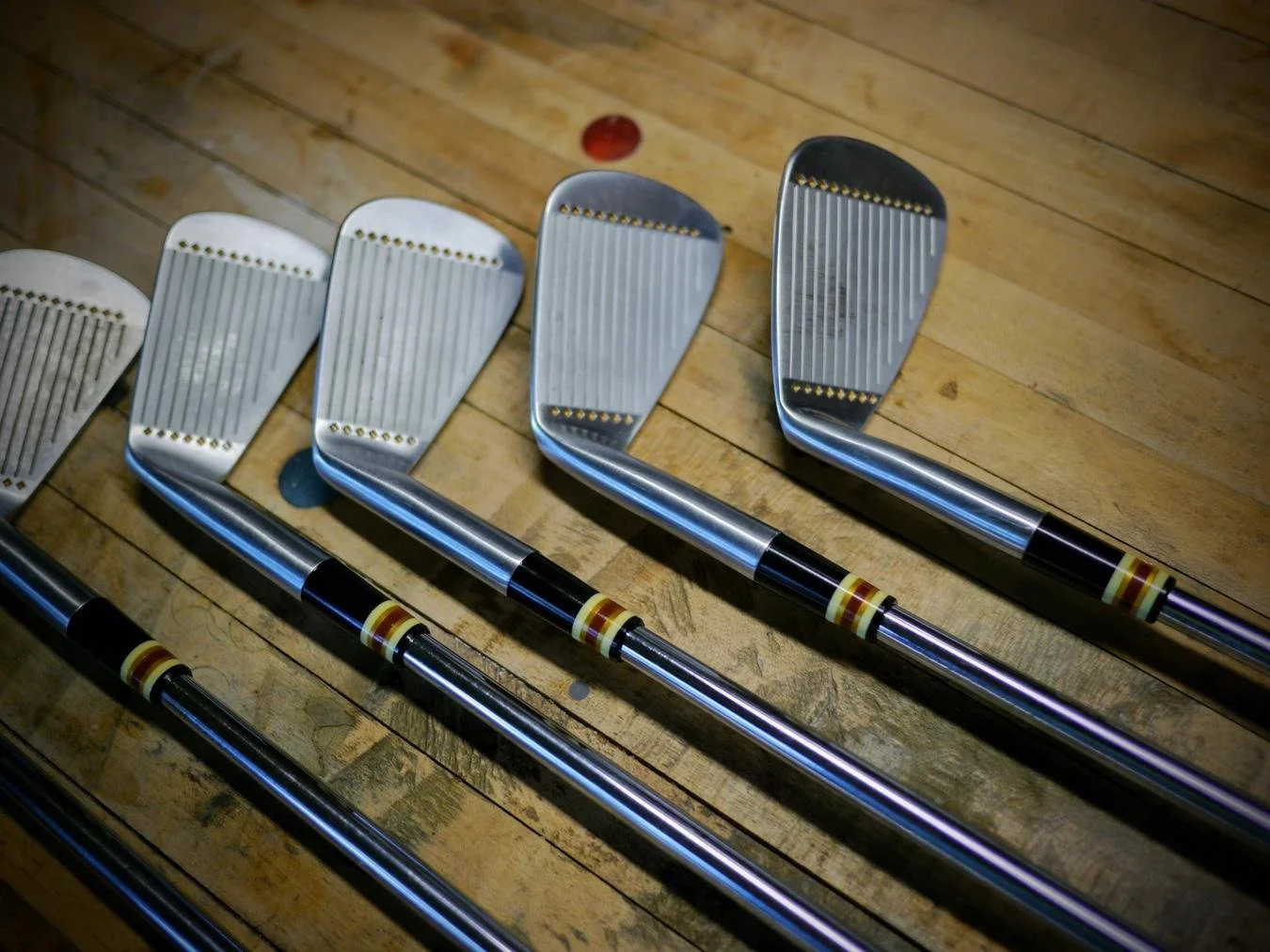 Six golf clubs arranged in a line on a wooden floor.