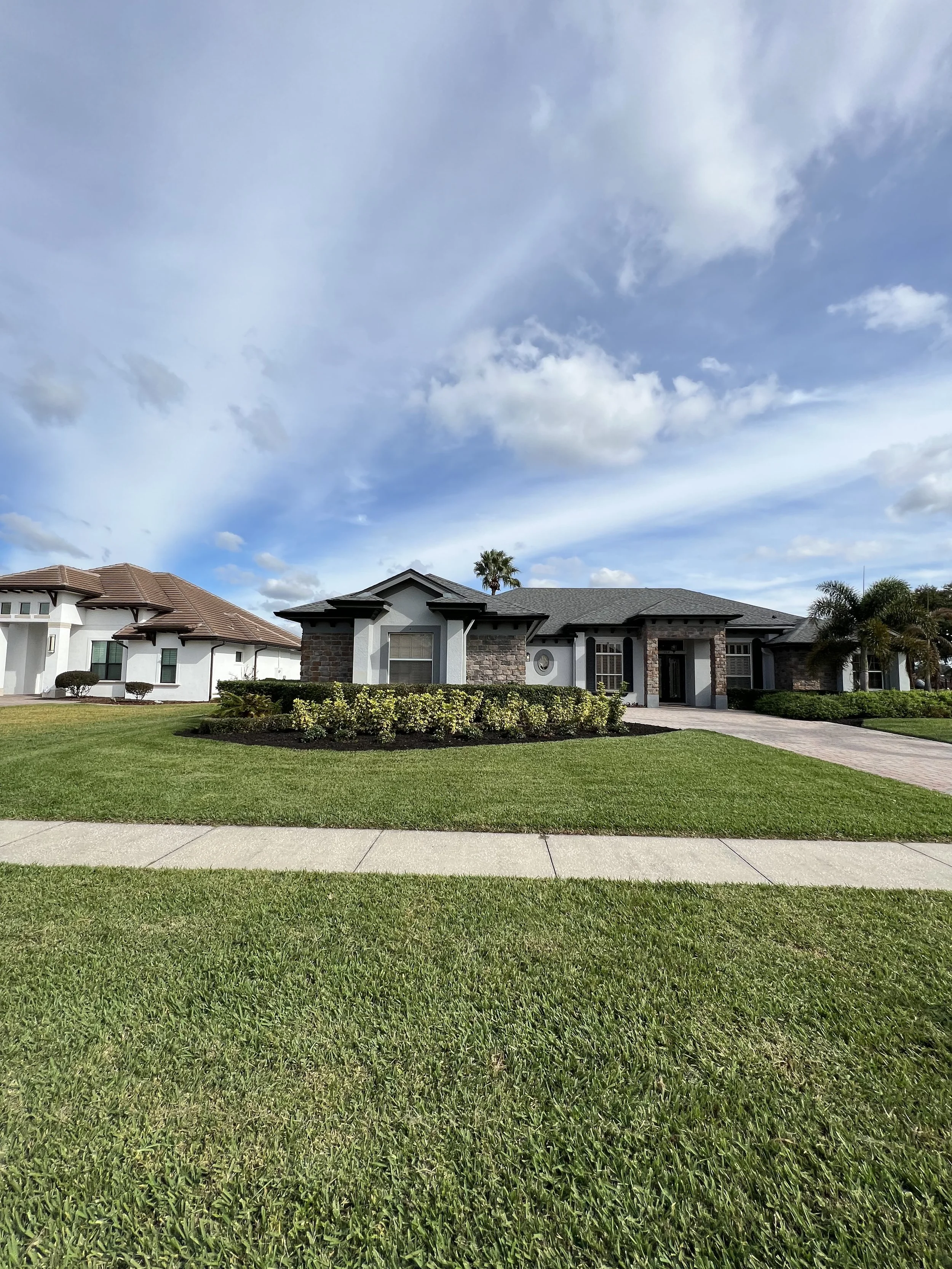 A suburban neighborhood with houses, a well-maintained lawn, and a partly cloudy sky.