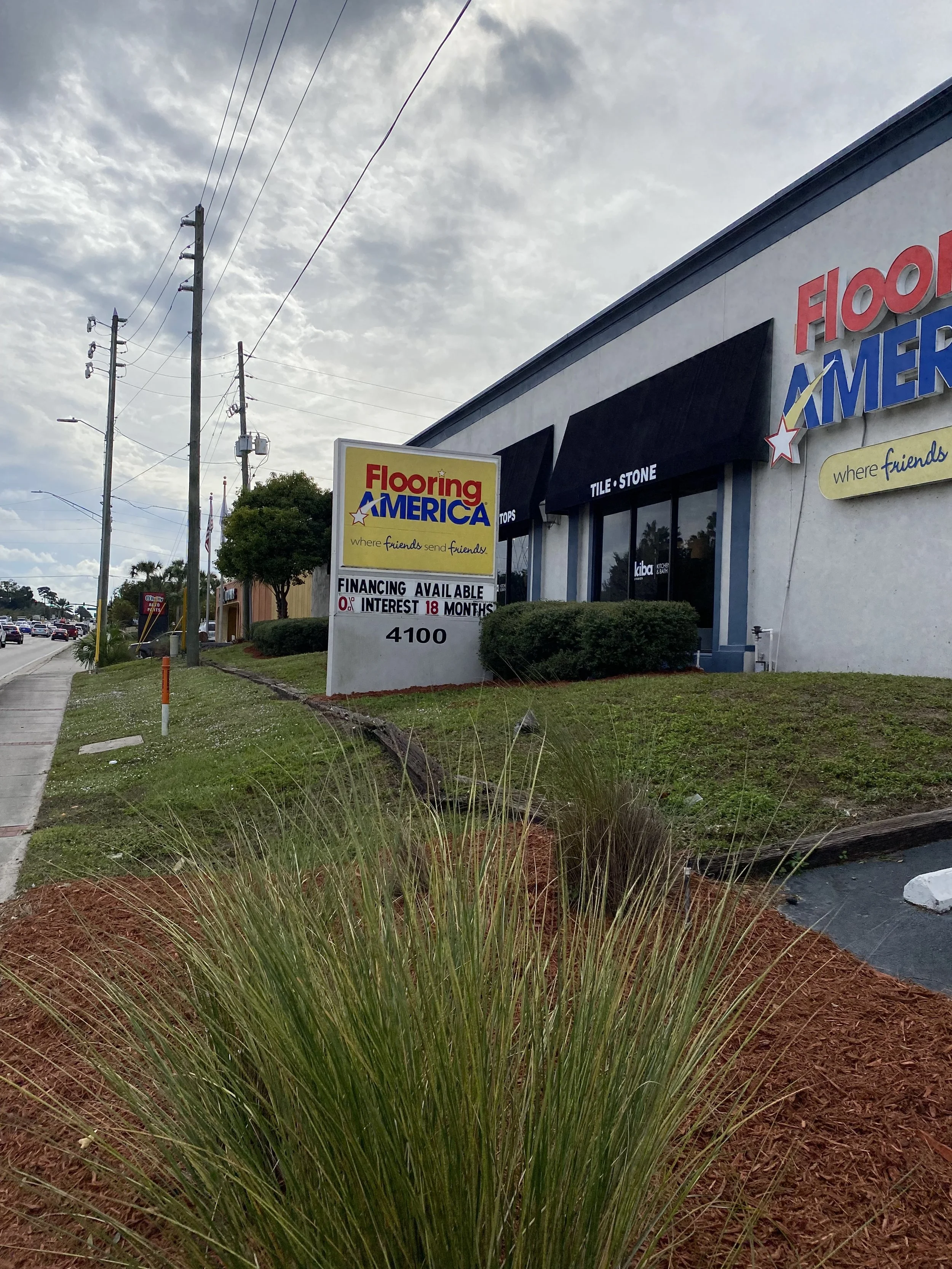 outside view of Flooring America store with signage and landscaping, including grass, shrubs, and power lines in the sky.