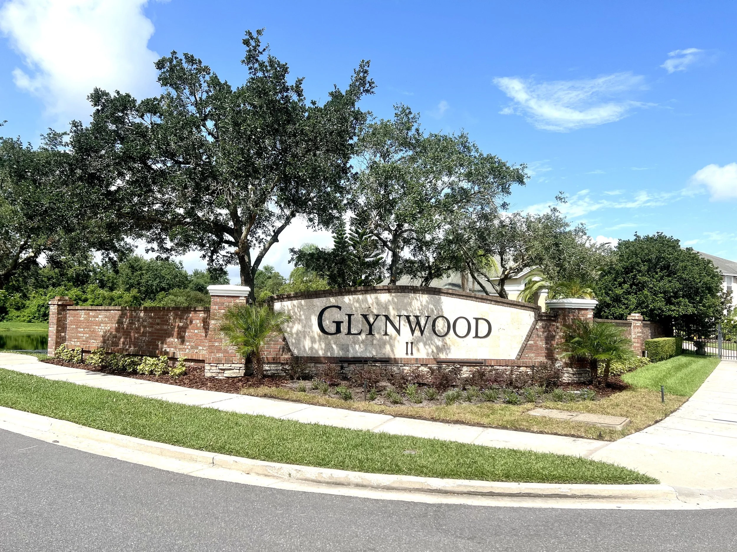 A brick wall entrance sign with the words 'Glynwood' and a few trees, with a partly cloudy sky overhead.