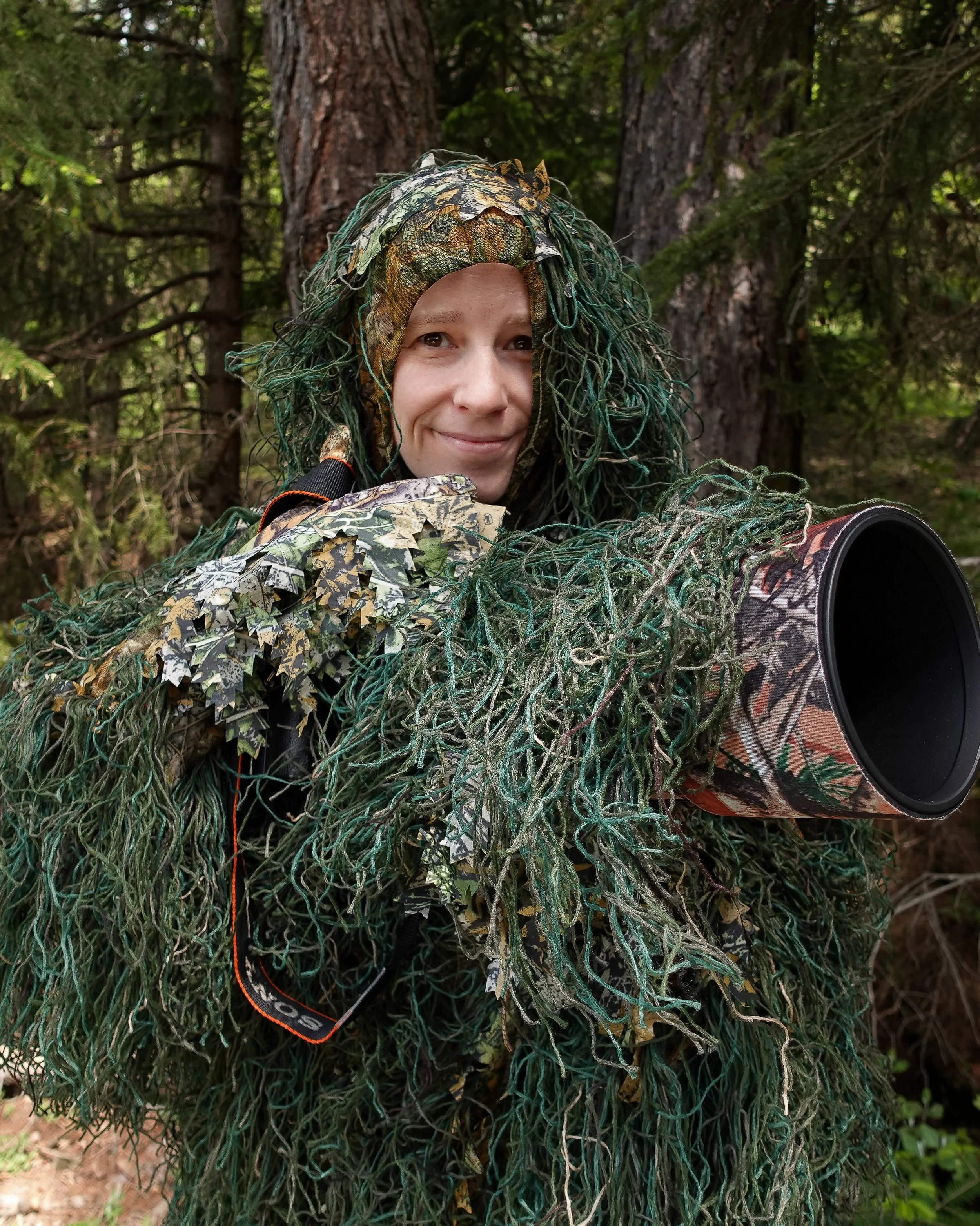 Wildlife-Fotografin Ariane Totzke im Tarnanzug mit Teleobjektiv im Wald – spezialisiert auf Natur- und Tierfotografie in freier Wildbahn