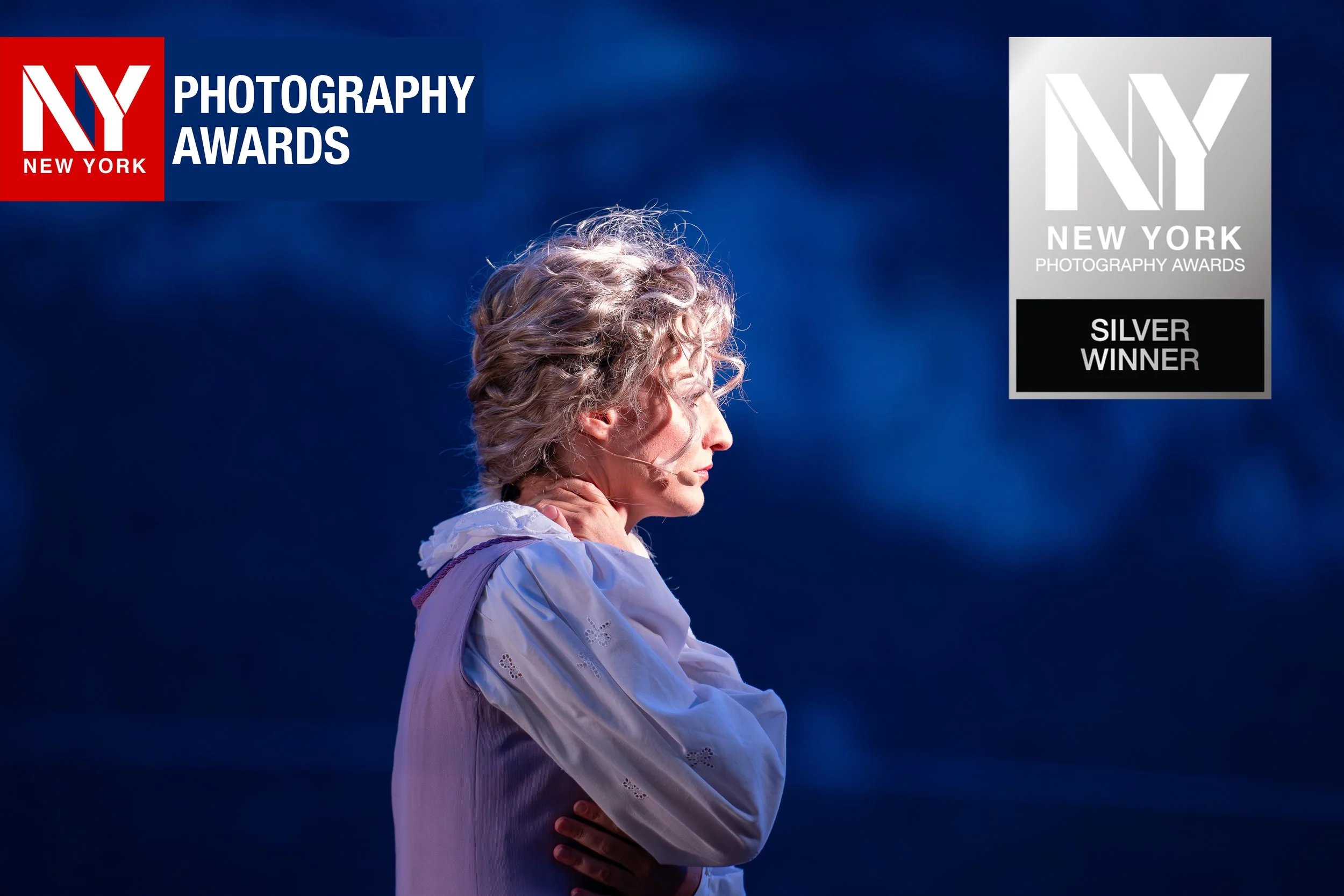 Eine Frau mit welligem grauem Haar, die nachdenklich den Kopf senkt, vor einem dunklen blauen Hintergrund, mit einem Logo der NY Photography Awards und einem Text, der sie als Silbergewinnerin zeigt.