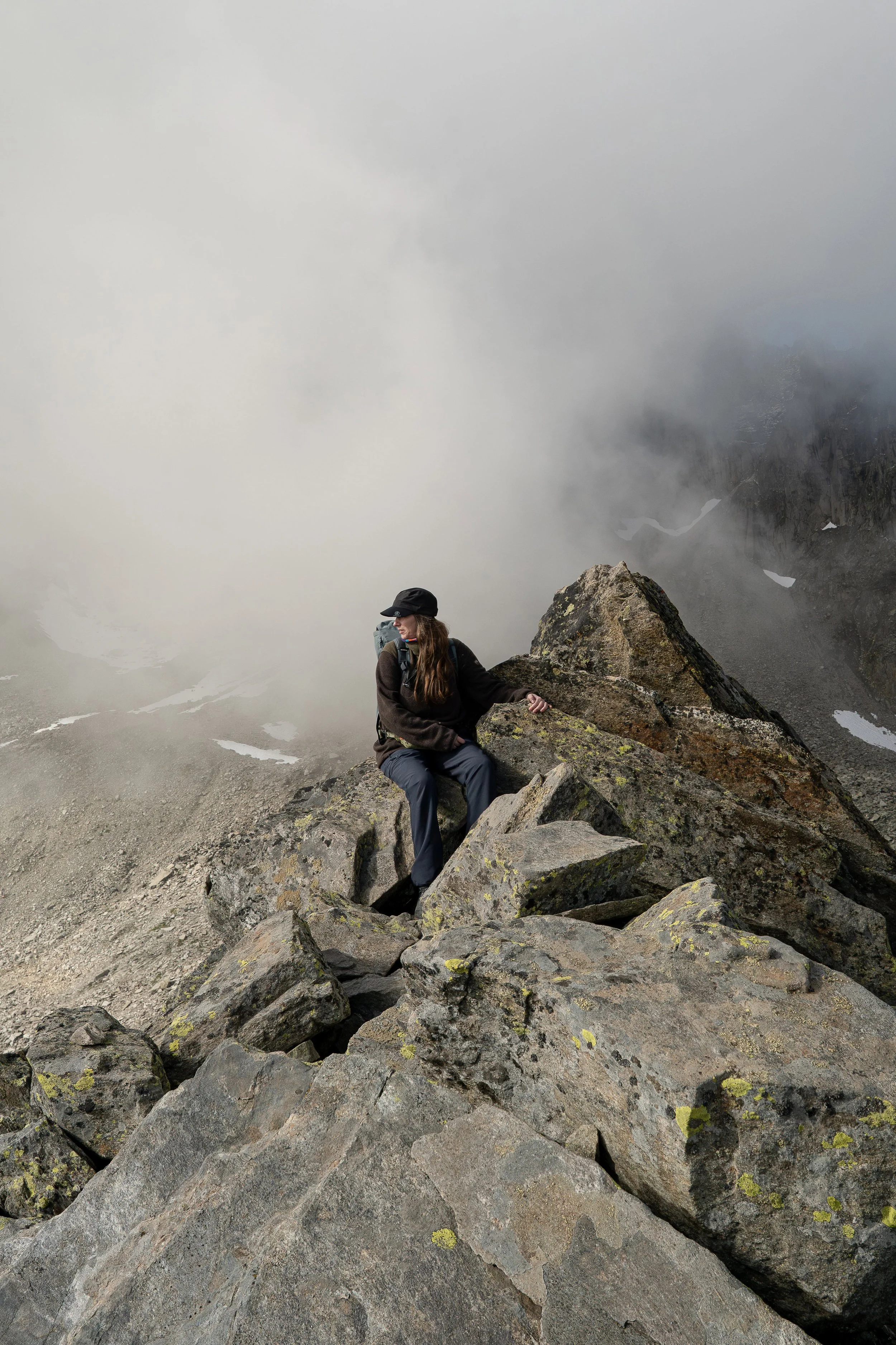 Wildlife- und Landschaftsfotografin Ariane Totzke während einer Steinbock-Fototour im Wallis. Sie sitzt auf Felsen in hochalpiner Landschaft, umgeben von schroffen Gipfeln, Nebel und Schneefeldern.