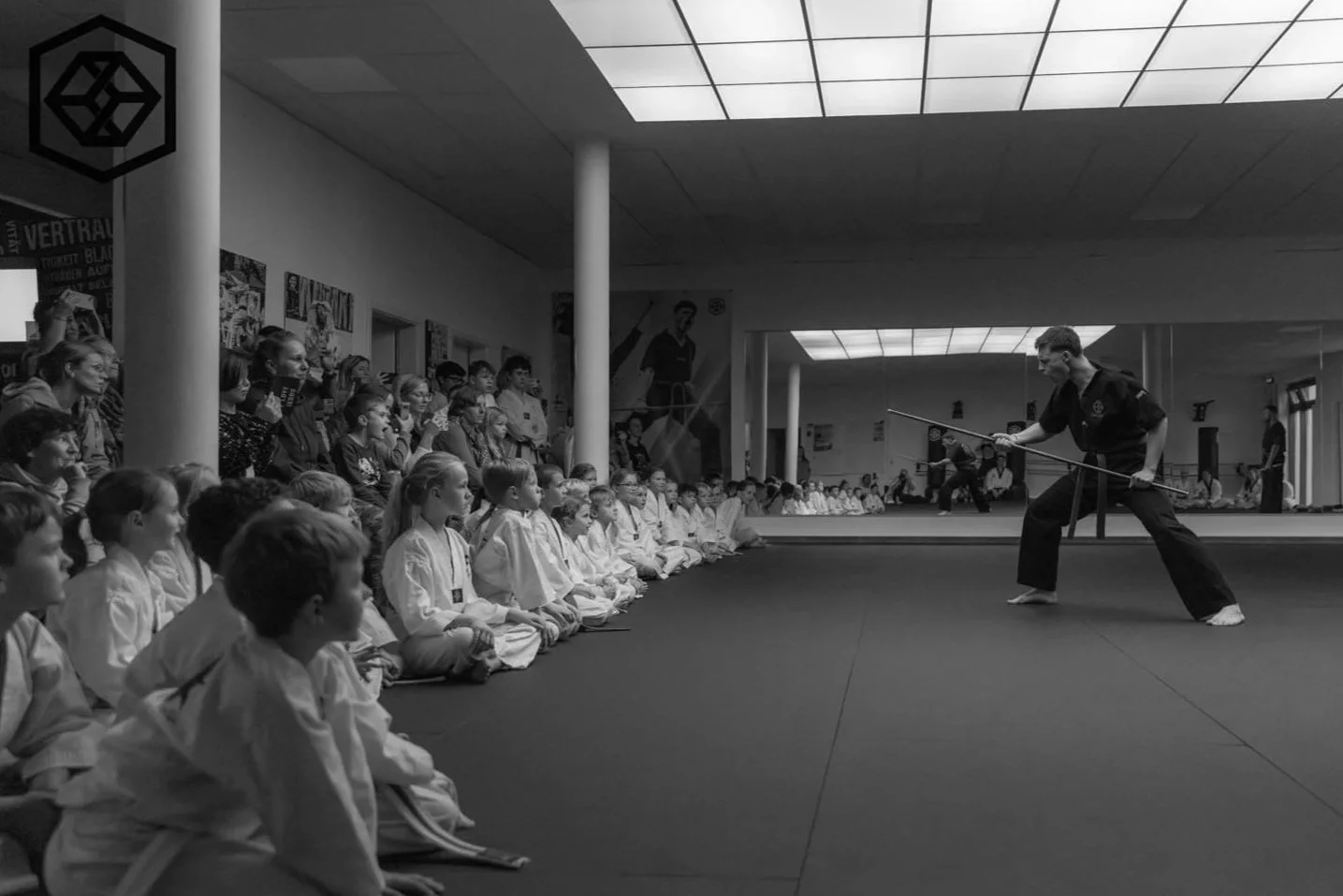 Martial arts Lehrer demonstriert Technik vor sitzenden Kindern in Turnhallenkonferenz.