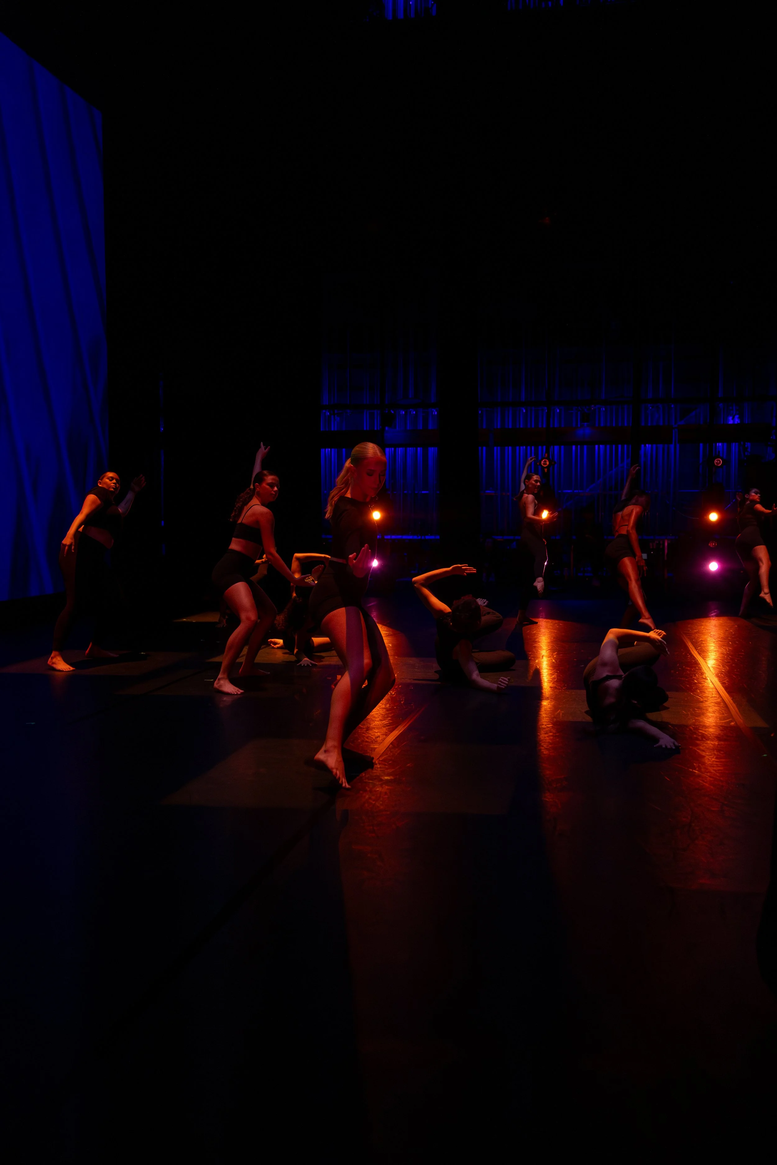 Dancers performing on stage with blue lighting and dark background.