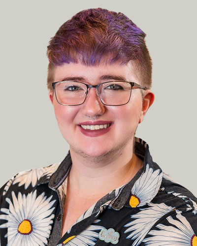 Person with short, two-toned purple and brown hair, wearing glasses, a septum piercing, and a black shirt with white daisies.