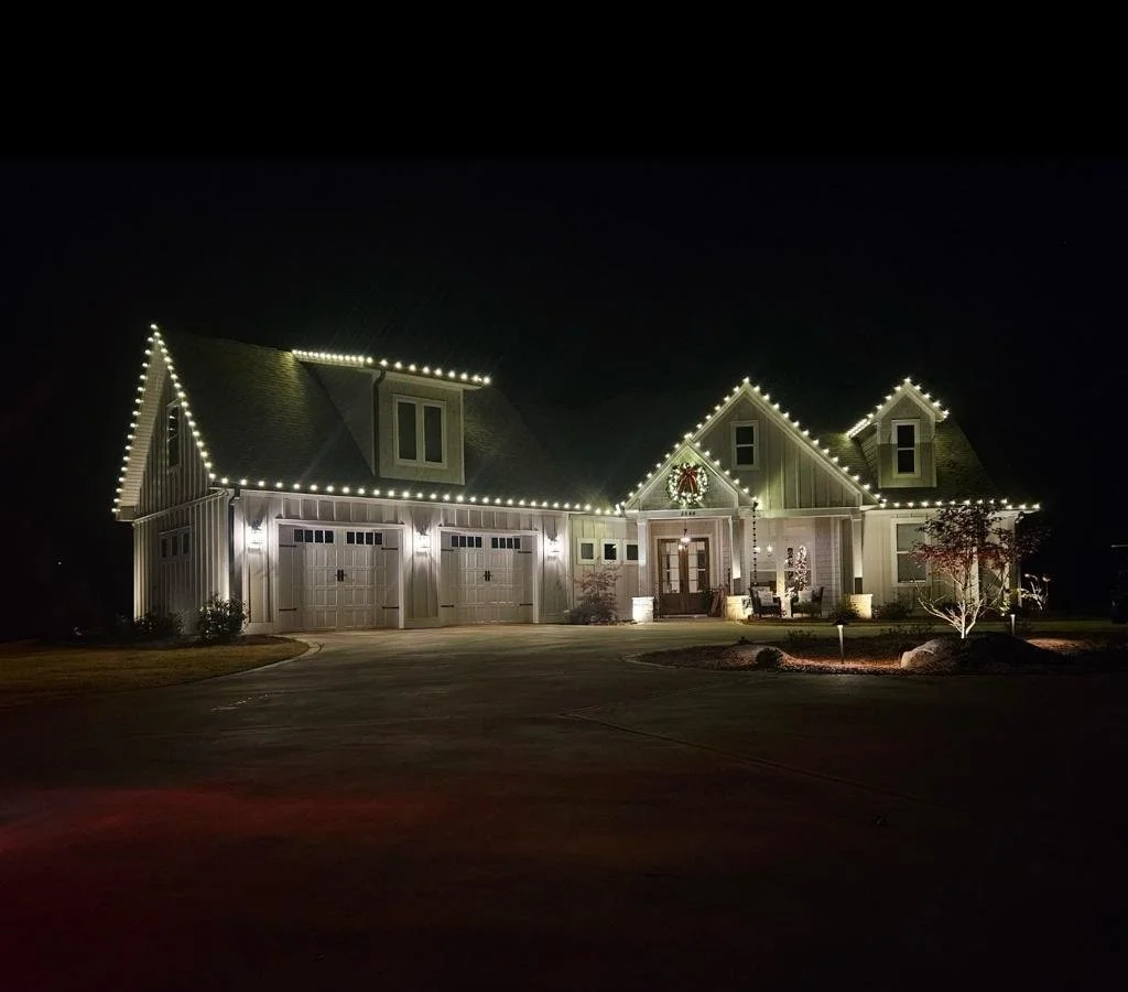 A house decorated with outdoor string lights and a wreath with a red bow on the front of the house at night.