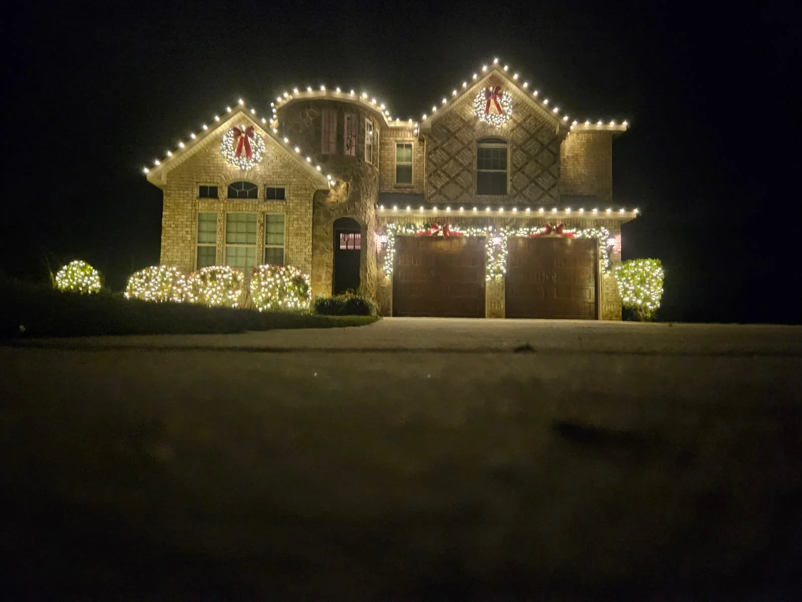 A two-story house decorated with Christmas lights and wreaths at night.