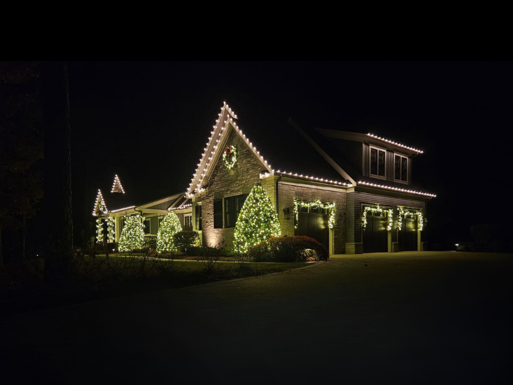 House decorated with Christmas lights at night, including a wreath and trimmed windows.