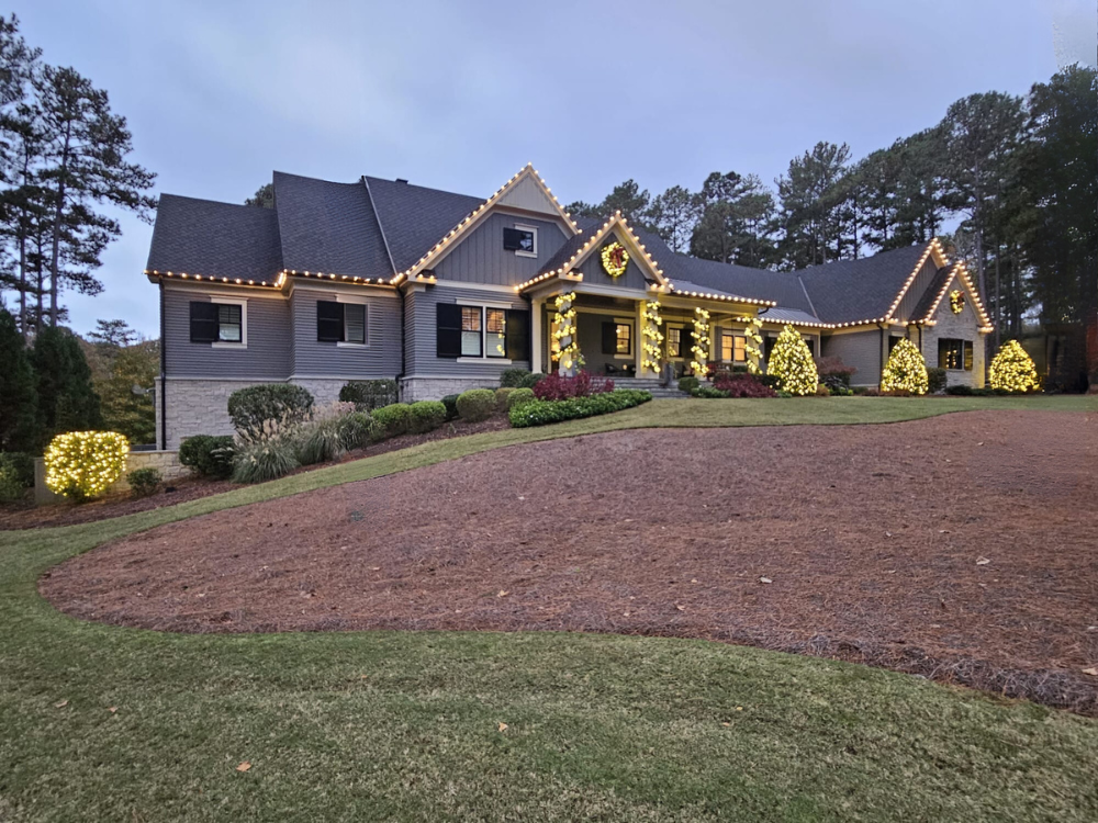 A large house decorated with holiday lights and wreaths, with a well-maintained lawn and trees in the background.
