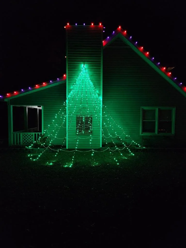 House decorated with green and multicolored Christmas lights, forming a Christmas tree shape on the front of the house.