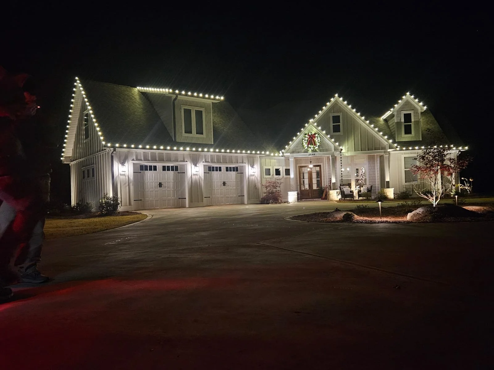 A house decorated with white Christmas lights along the roofline and a wreath with a red bow on the front door, illuminated at night.