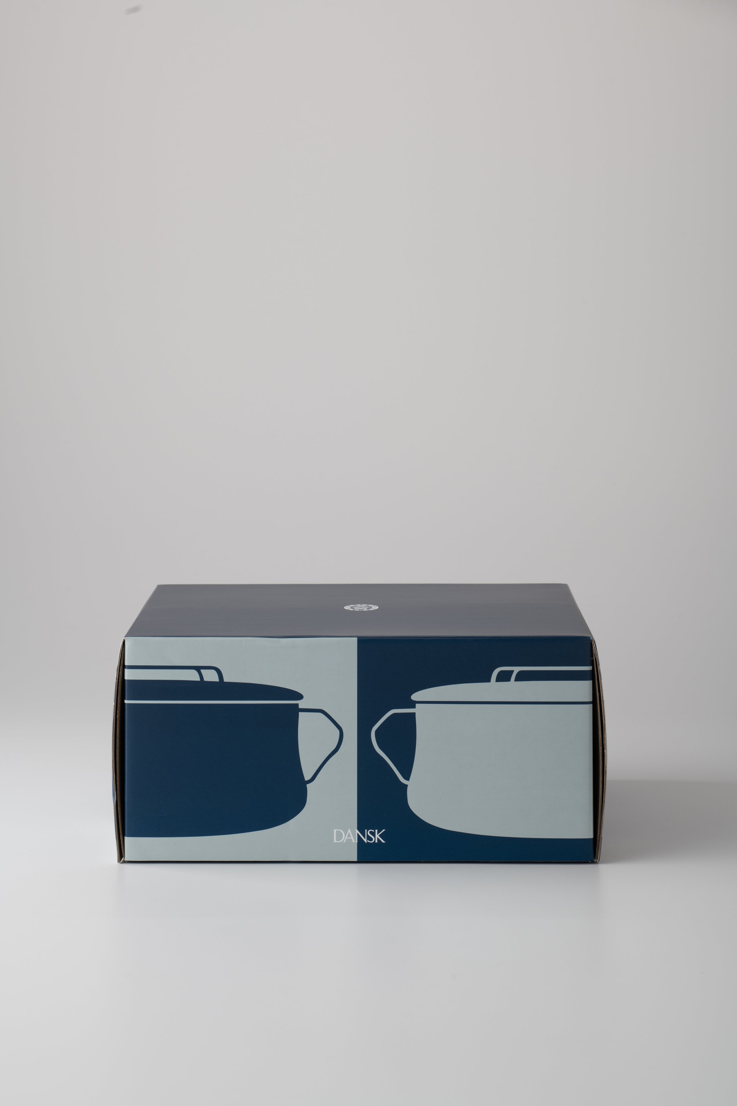 A cardboard box with a graphic of two navy blue glasses on the front, set against a plain grey background. The box has the text "DANSK" at the bottom.